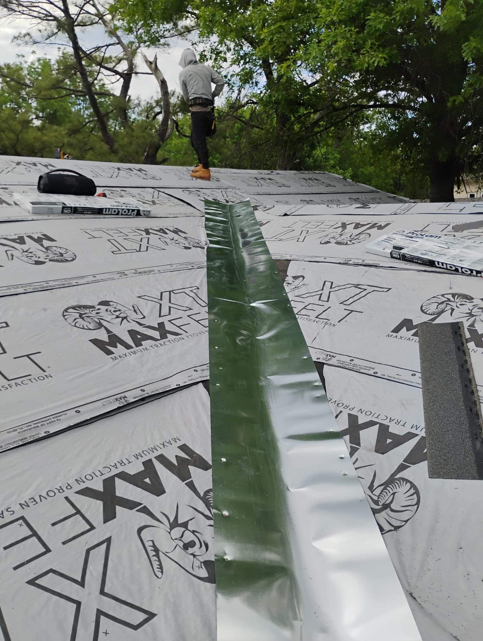A man is standing on top of a roof with trees in the background.