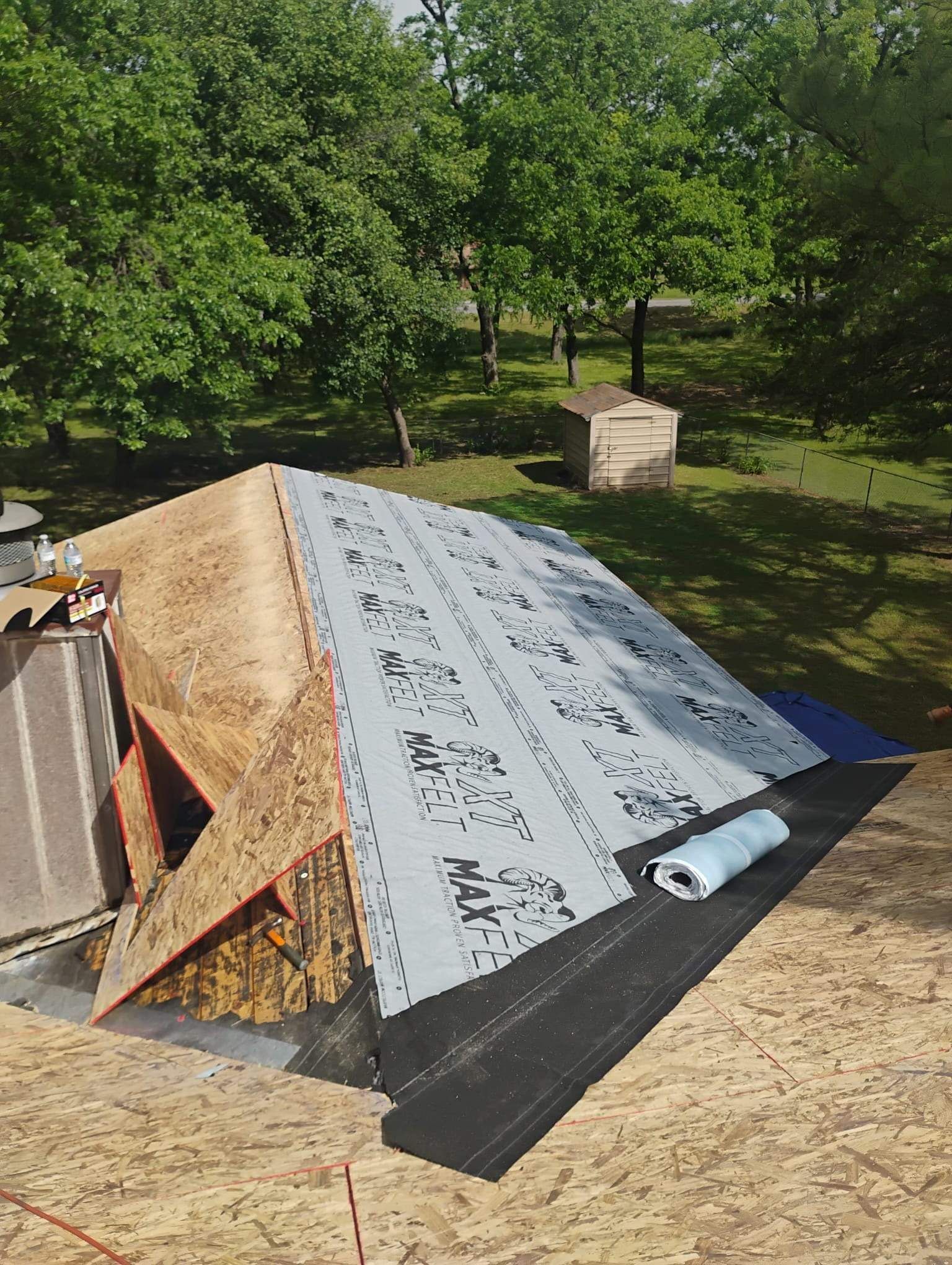 A roof is being built in a backyard with a lot of trees in the background.