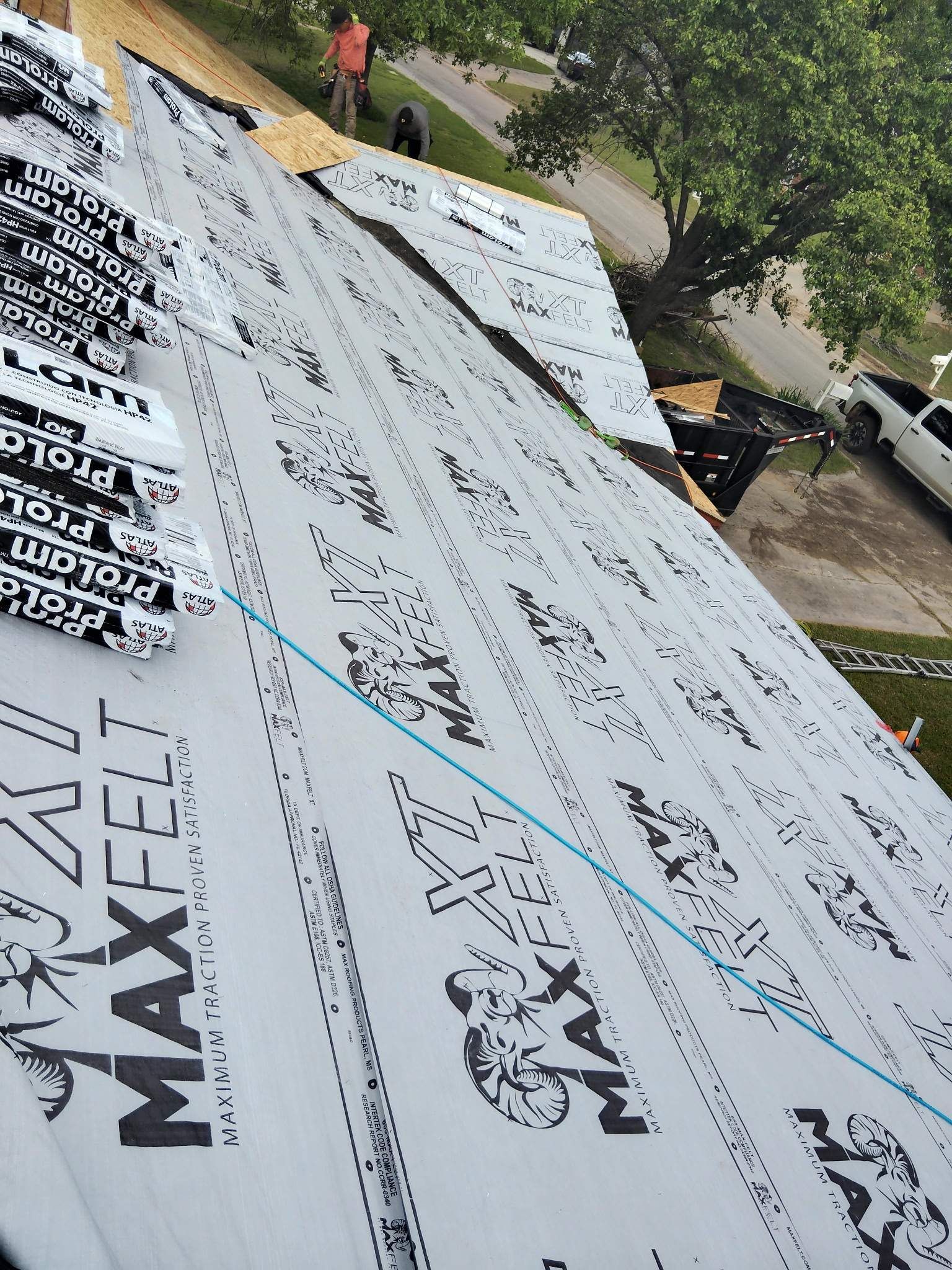 A white truck is parked on the side of the road next to a roof that is being worked on.