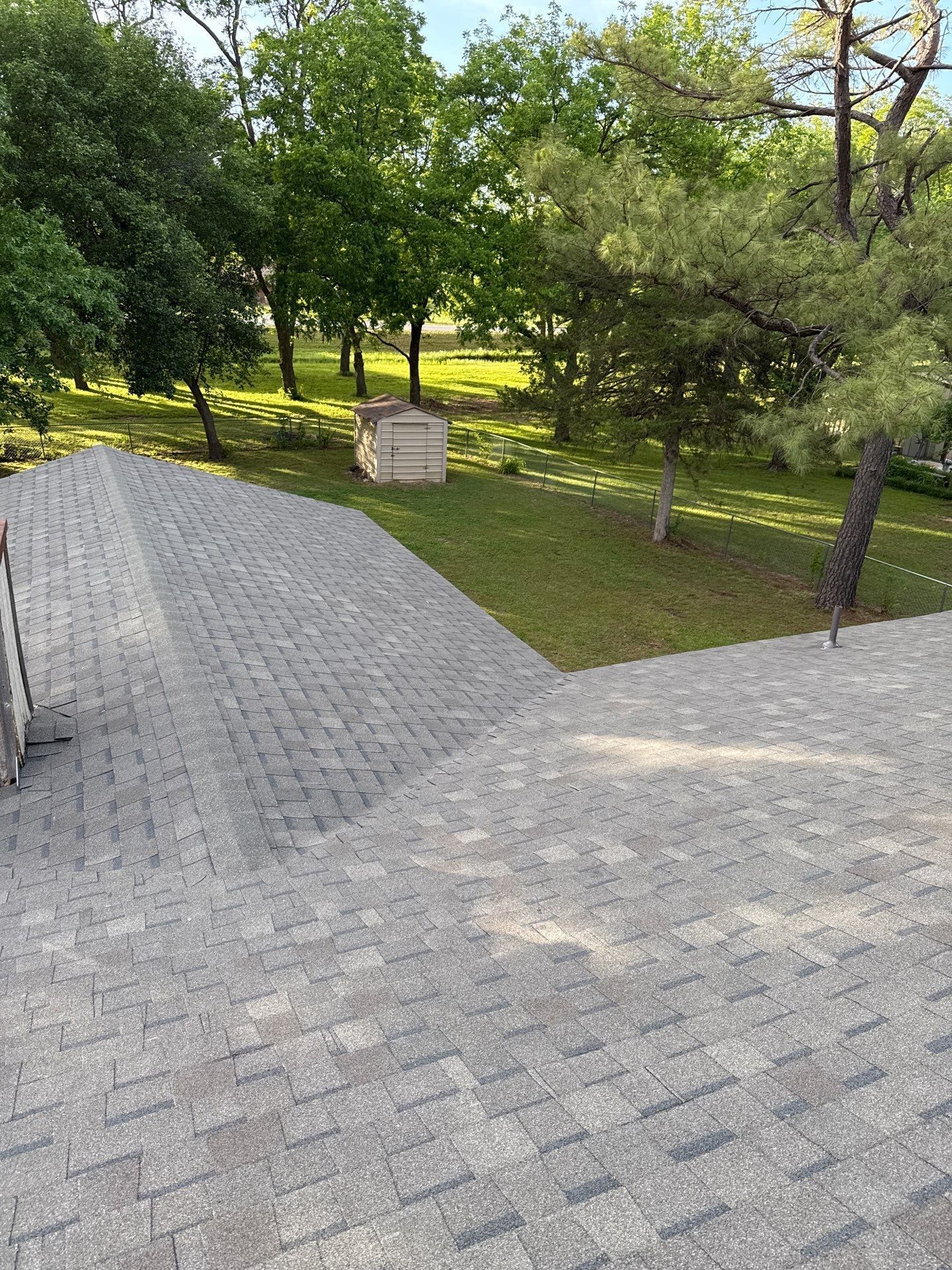 A roof with a ladder on it is surrounded by trees and grass.