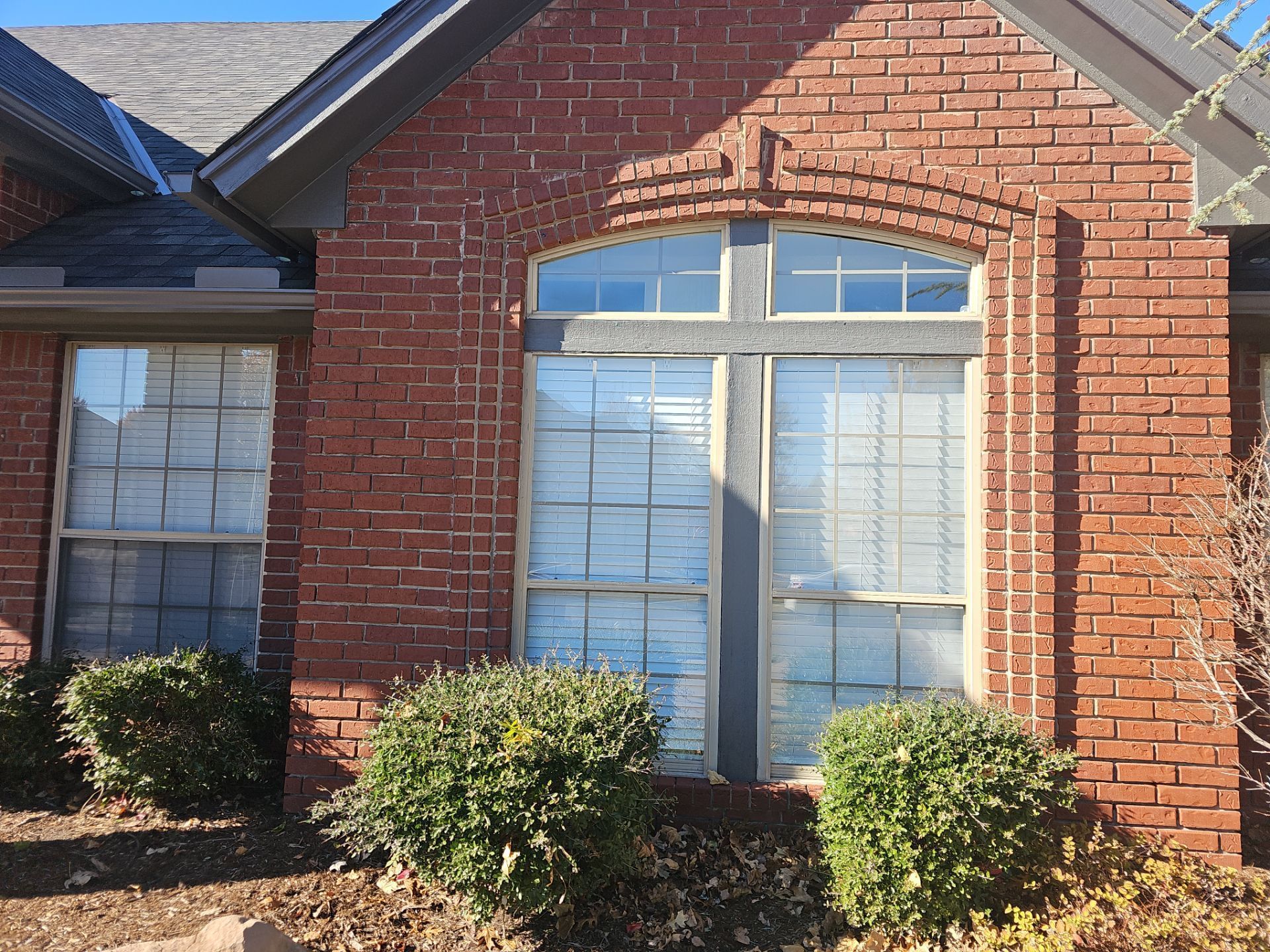 A brick house with a large window and bushes in front of it