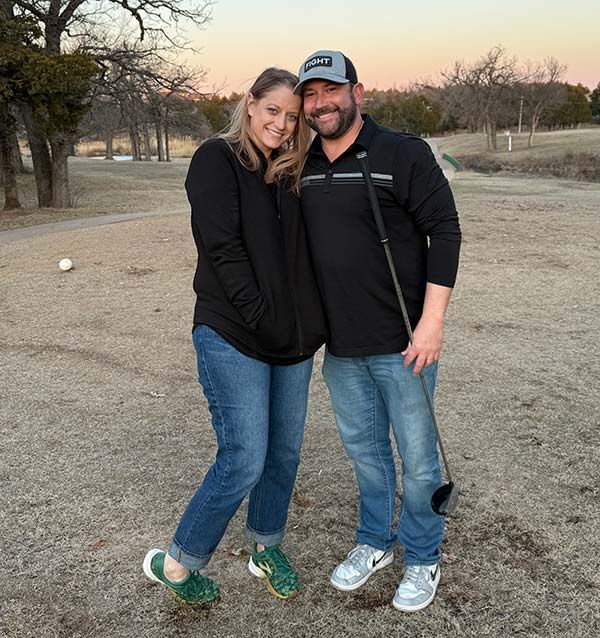 A man and a woman are posing for a picture on a golf course