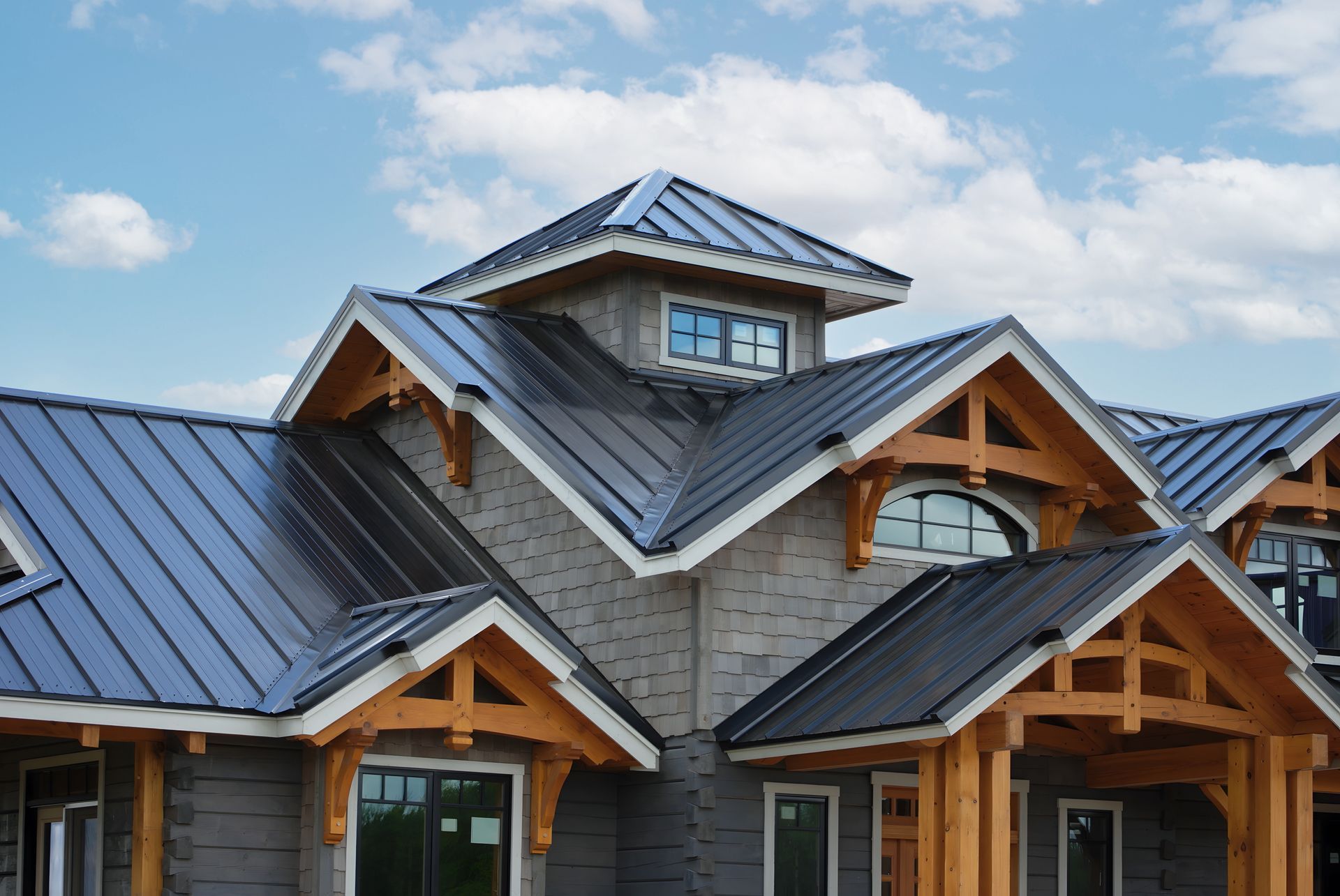 Gray house with a dark metal roof, wooden trim, and blue sky.