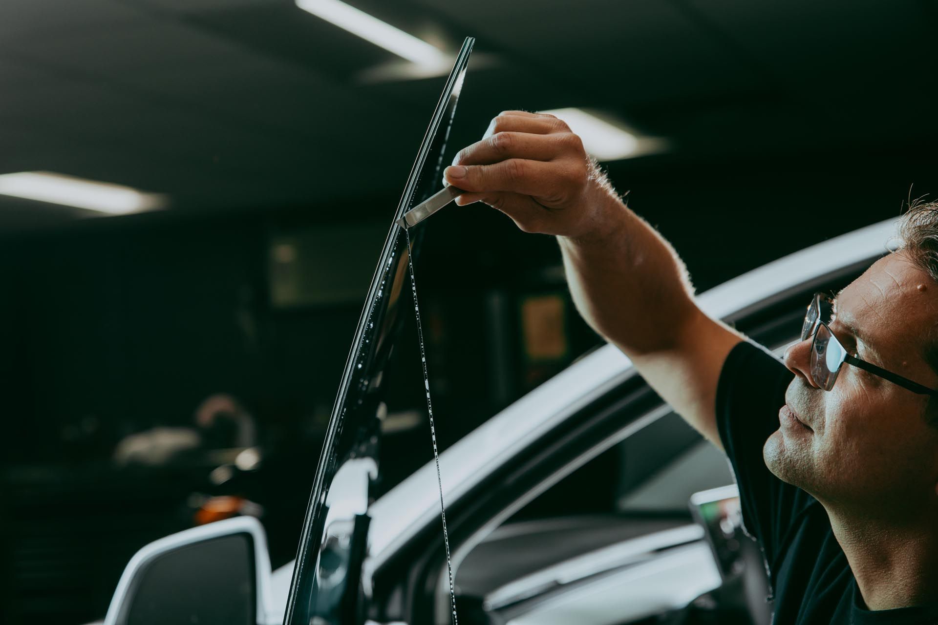 Man in glasses installing tint on car window.