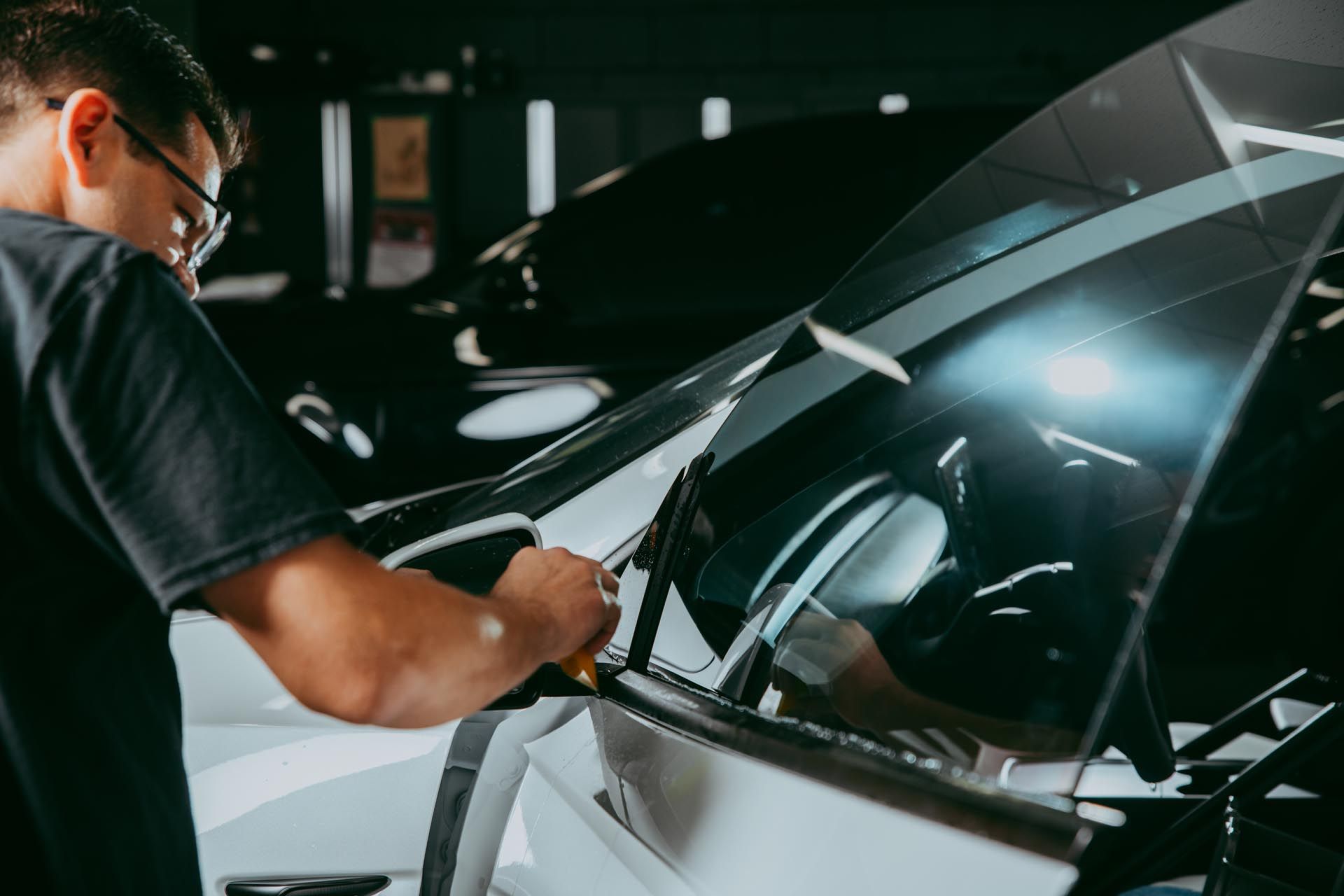 A person applying tint to a car window inside a garage.