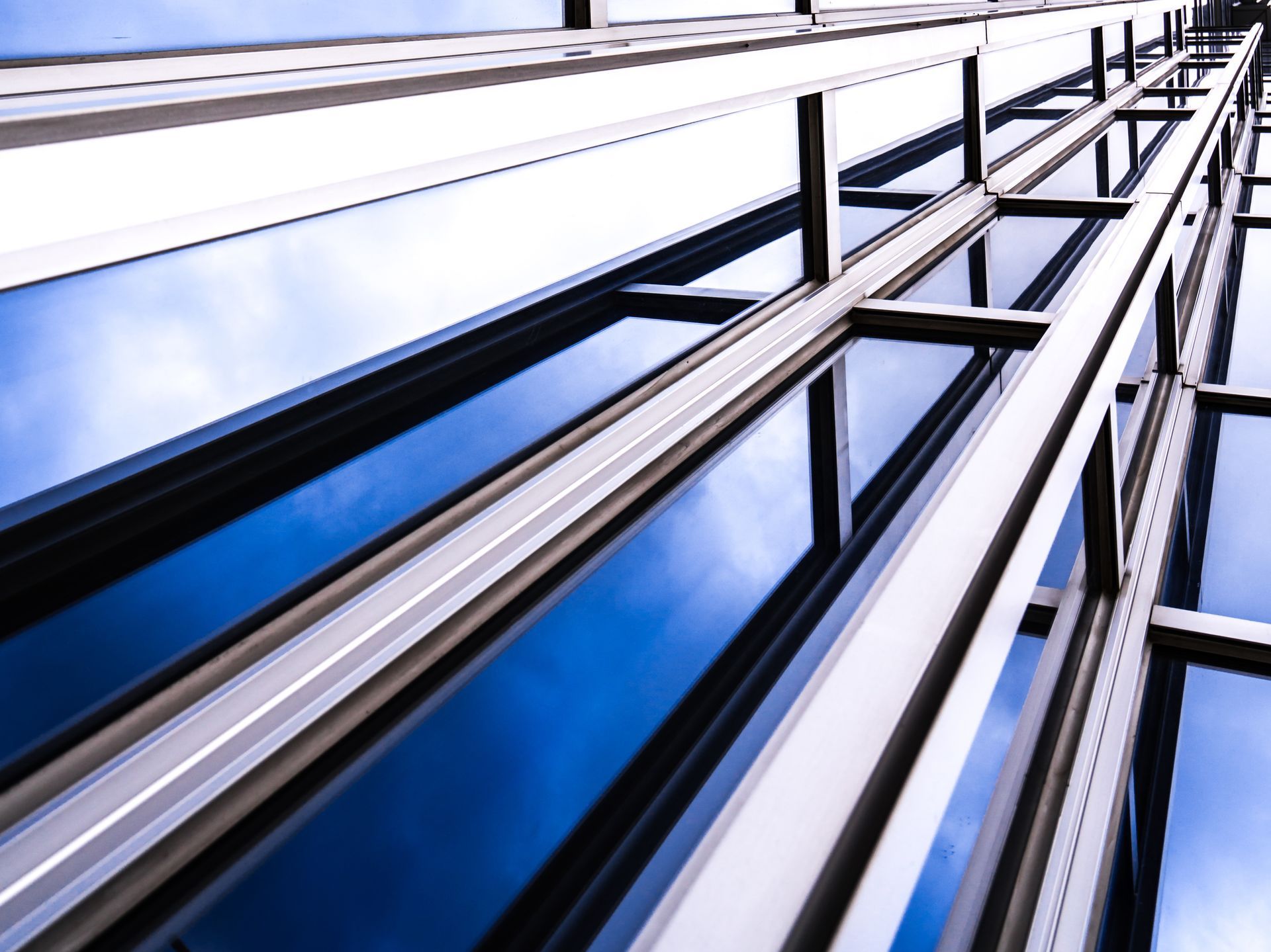 Blue-tinted windows on a modern building; sky reflected.