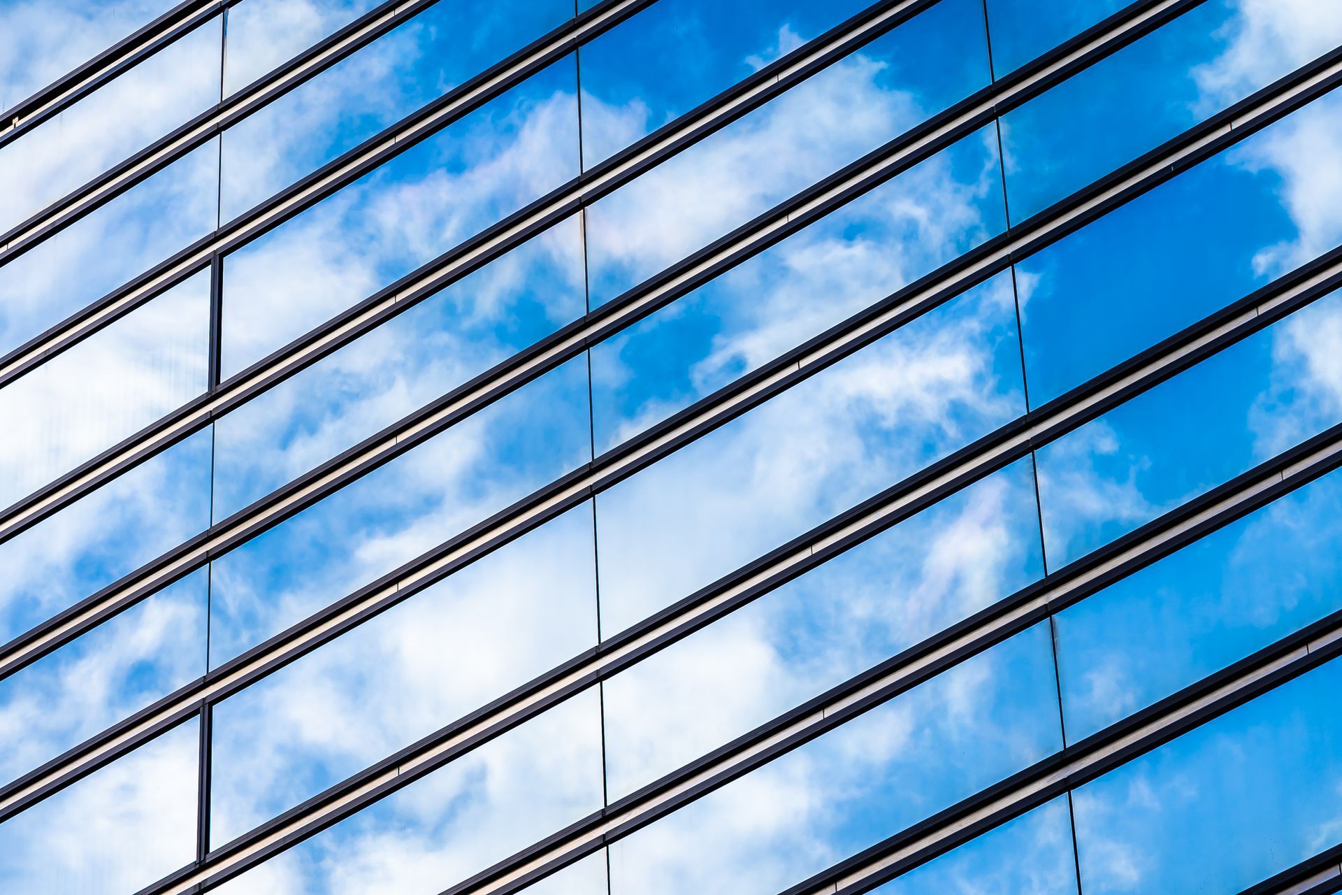 Glass skyscraper reflecting a bright blue sky with fluffy white clouds.