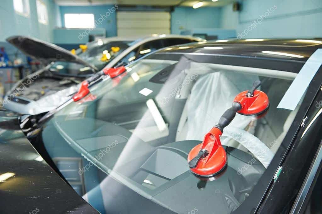 Windshield being worked on at an auto repair shop, held with red suction cups.