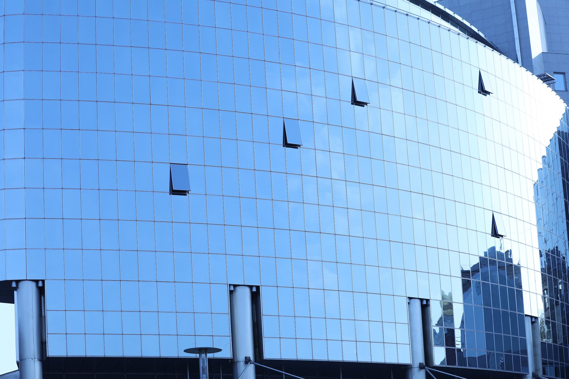 Blue glass facade of a modern building, reflecting the sky, with a curved shape and some visible windows.