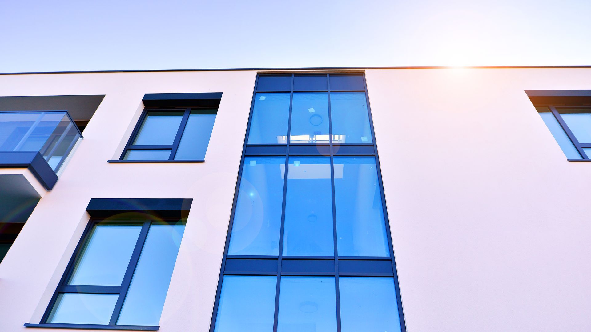 Modern white building with blue-tinted glass windows and a bright sunlit sky.