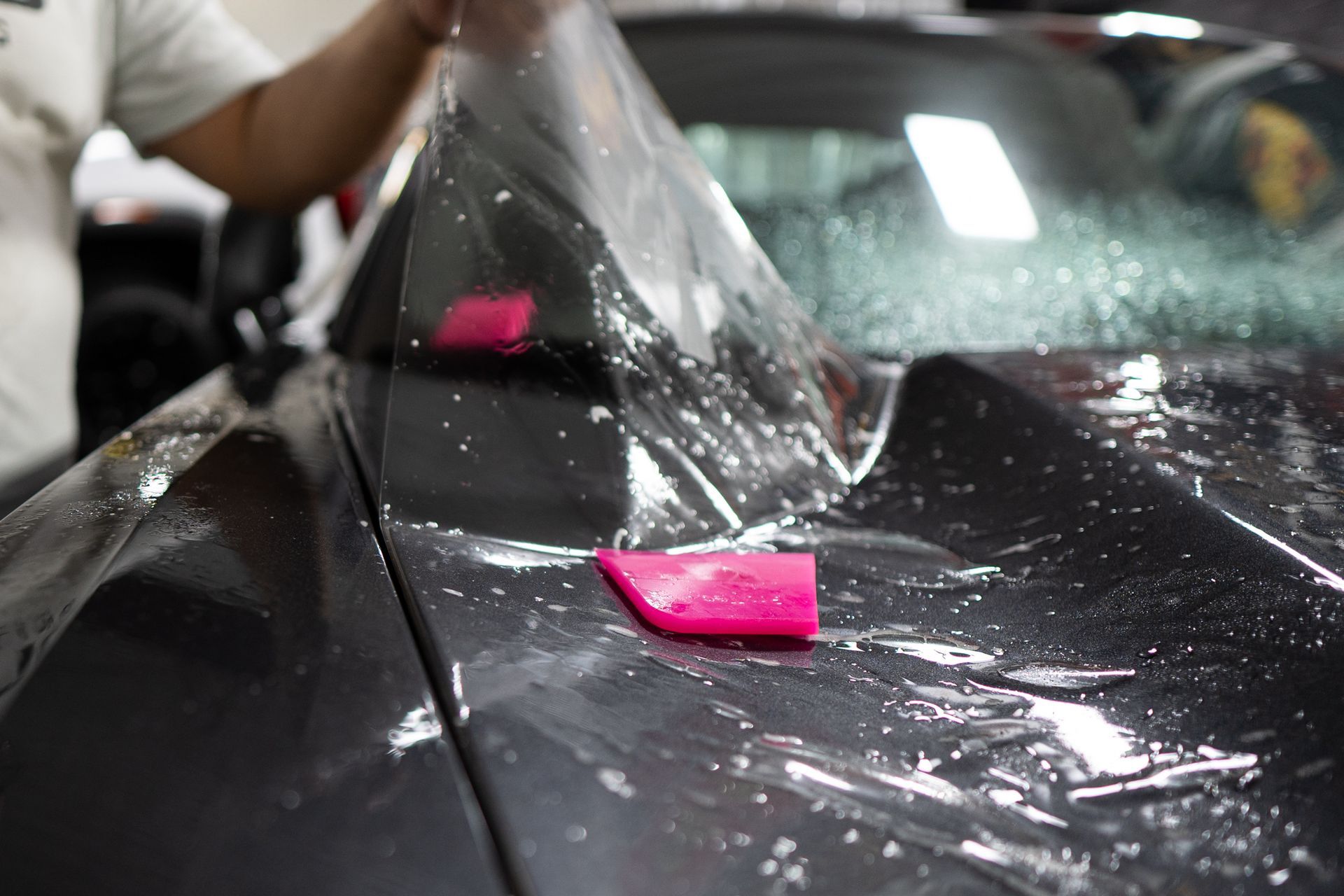 Person applying clear protective film to a car's hood with a pink squeegee.