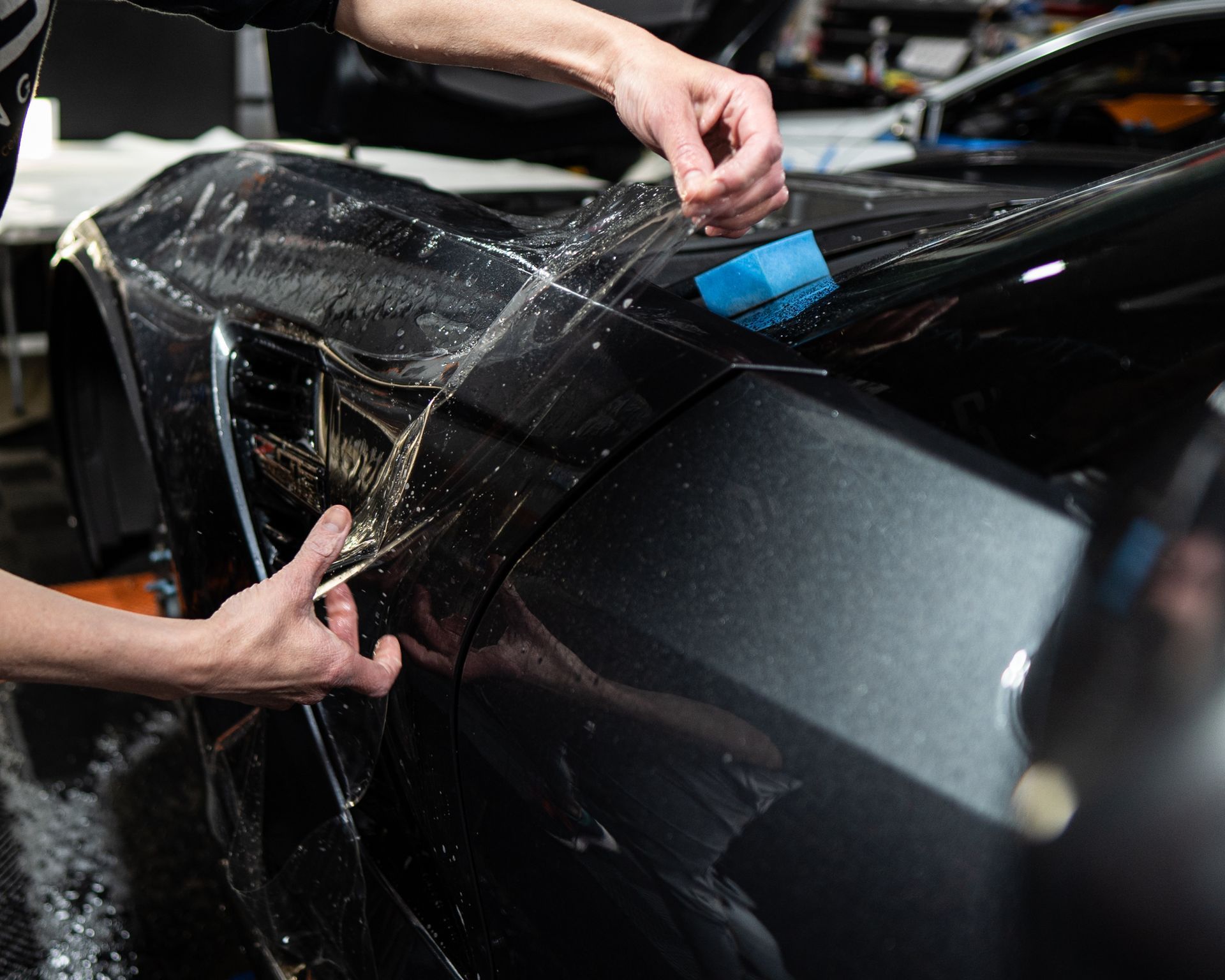 Hands applying clear protective film to a black car's fender.