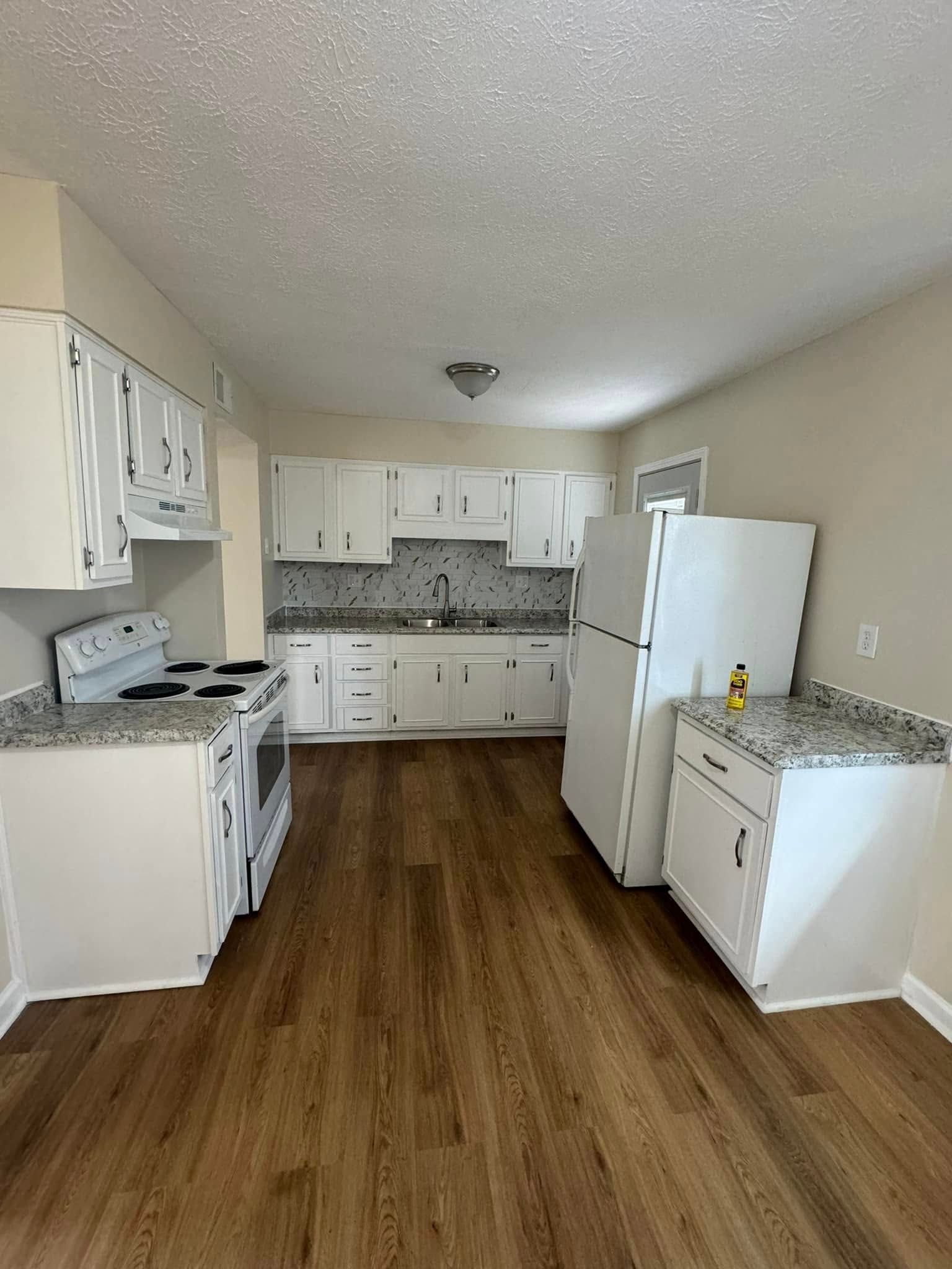 A kitchen with white cabinets , a refrigerator , a stove , and a sink.