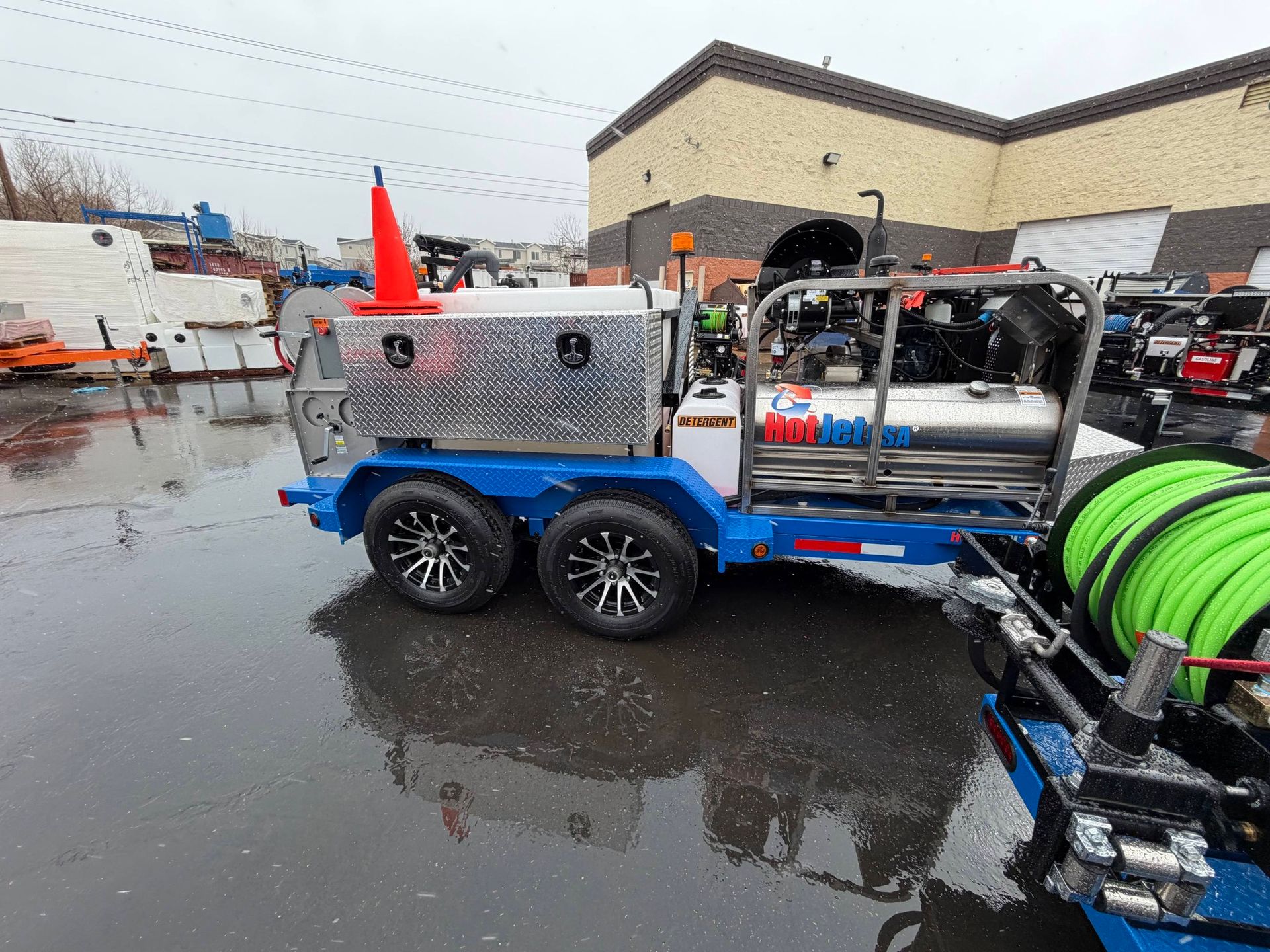 Blue utility trailer with equipment and bright green hose in a wet parking lot