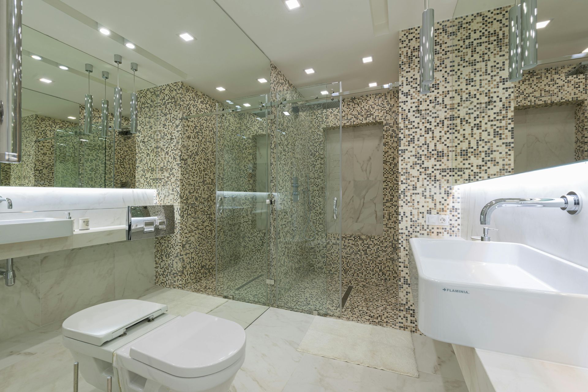 Modern tiled bathroom with two sinks, toilets, mirrors, and glass shower stalls