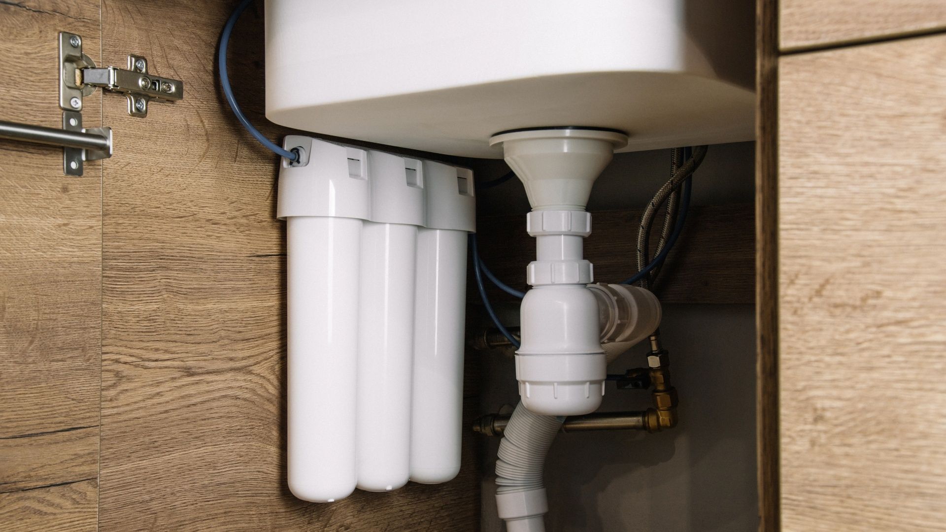 Under-sink water filtration system with white canister filters and plumbing under a sink