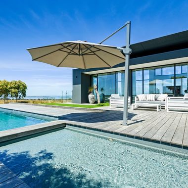A large umbrella is hanging over a swimming pool in front of a house — Azure Pools Mid North Coast In Taree, NSW