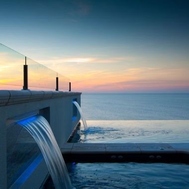 A swimming pool with a waterfall and a view of the ocean at sunset — Azure Pools Mid North Coast In Taree, NSW