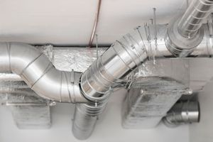 Silver metal HVAC ductwork and pipes installed against a white ceiling.