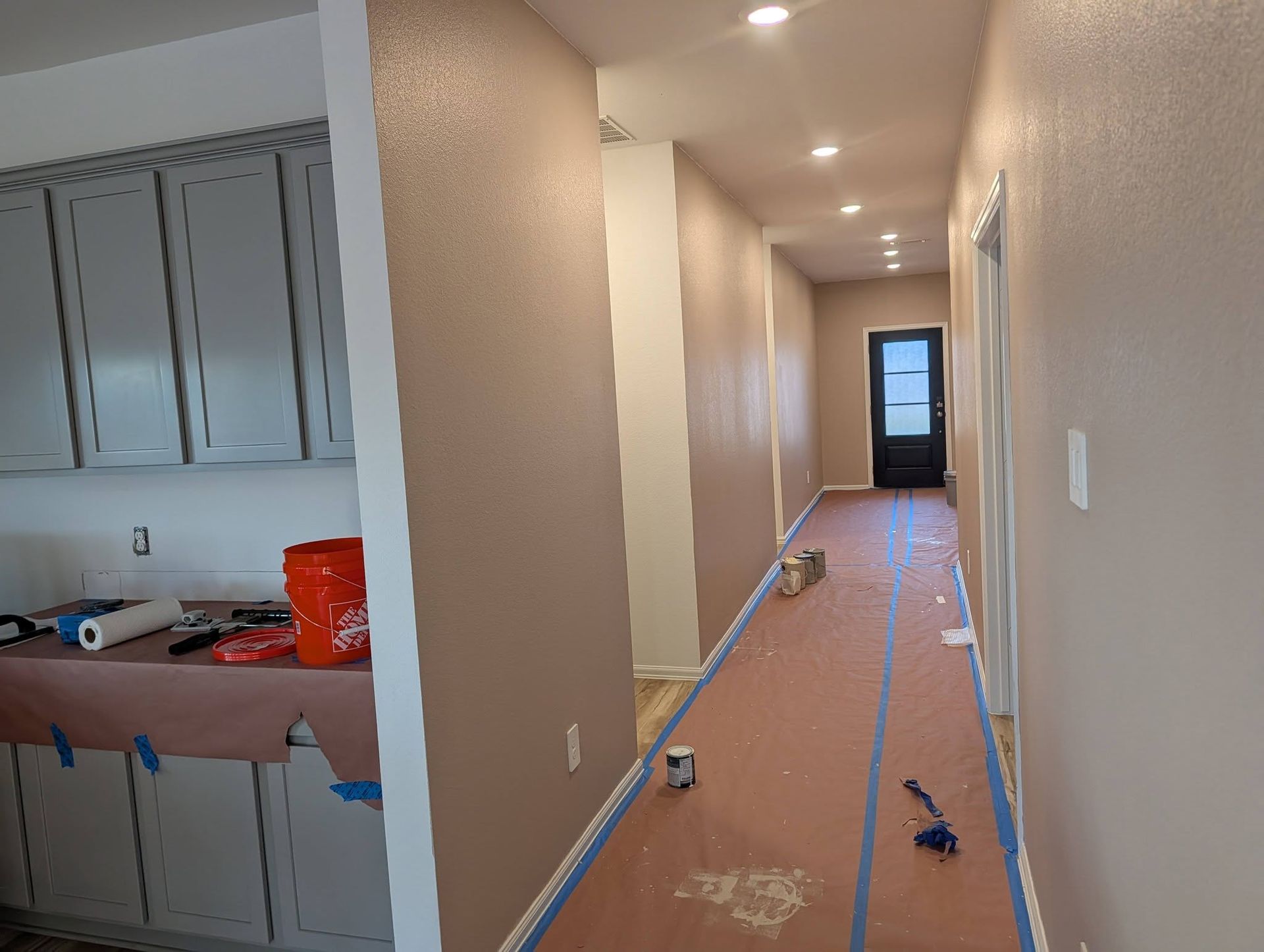 An interior hallway under renovation, with protective paper on the floor, grey cabinets on the left, and a dark back door.