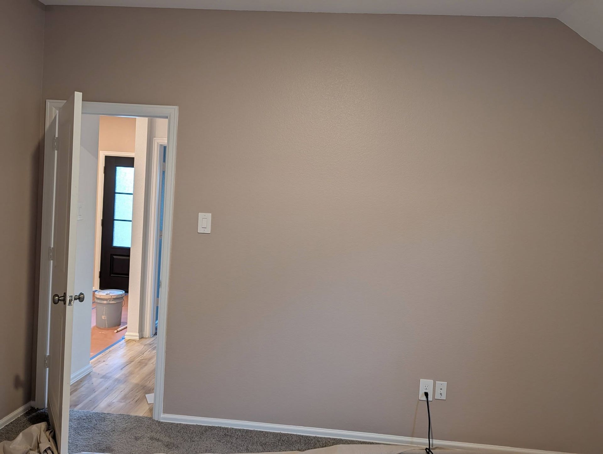 A plain light-brown interior wall with a white doorway, white trim, and a power outlet.