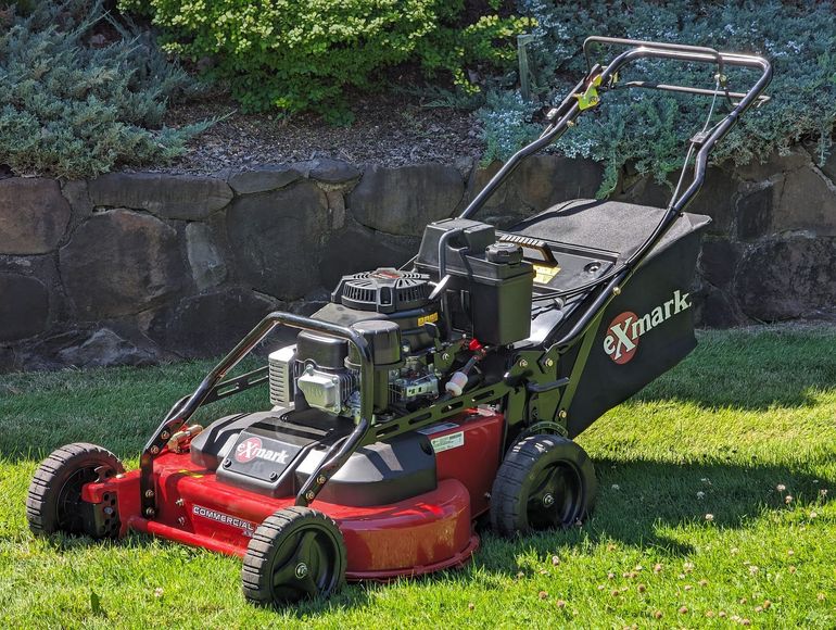 A red and black lawn mower is sitting on top of a lush green lawn.