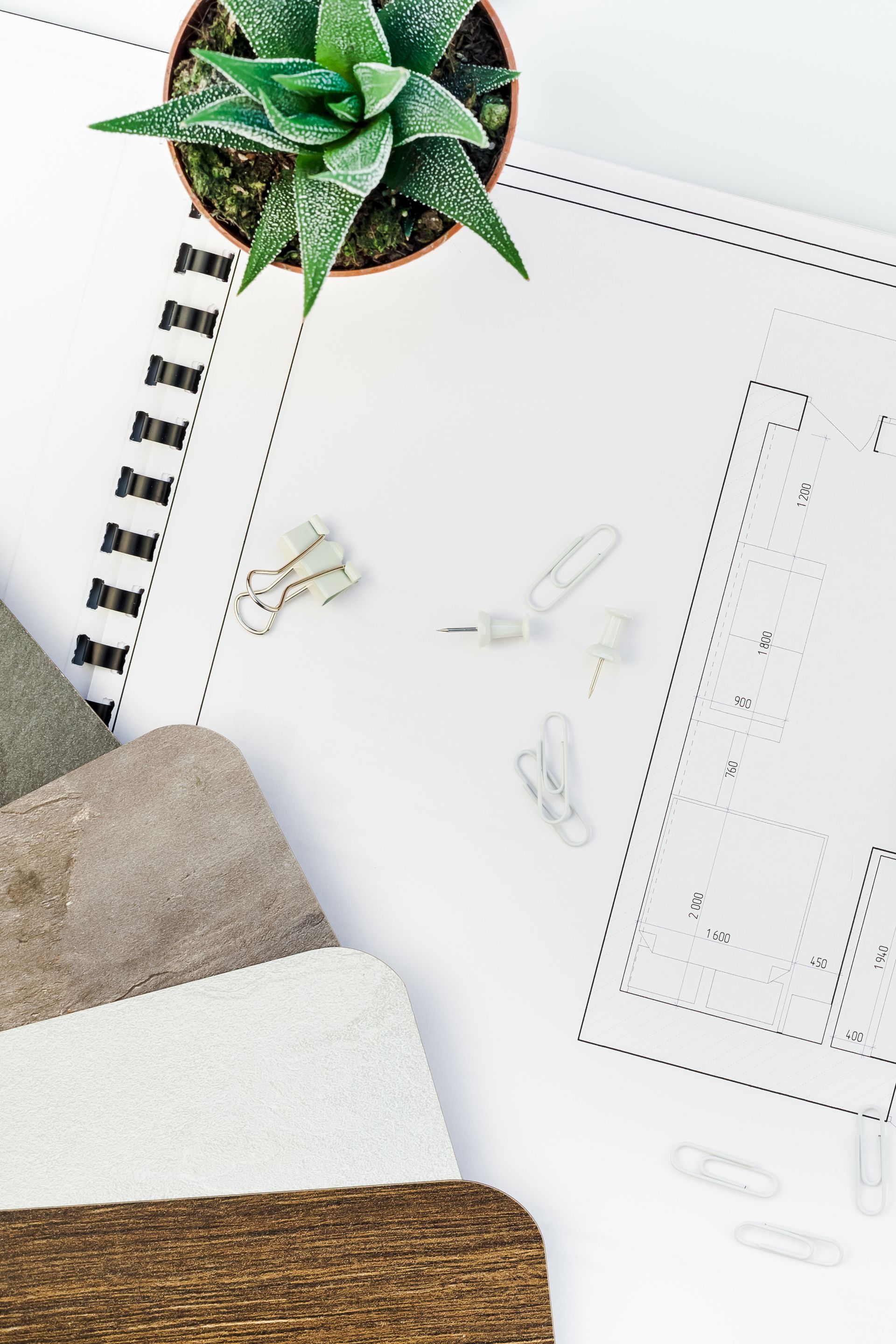 Disposizione piatta: scrivania di un architetto con pianta, planimetria, campioni di carta e graffette su una superficie bianca.