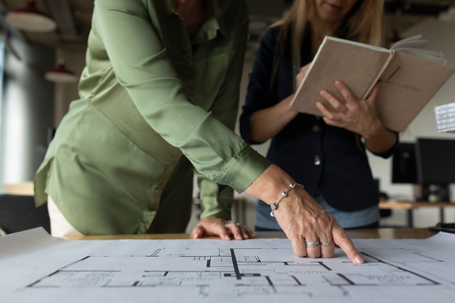 Due donne esaminano progetti architettonici, una delle quali indica, in un ufficio.