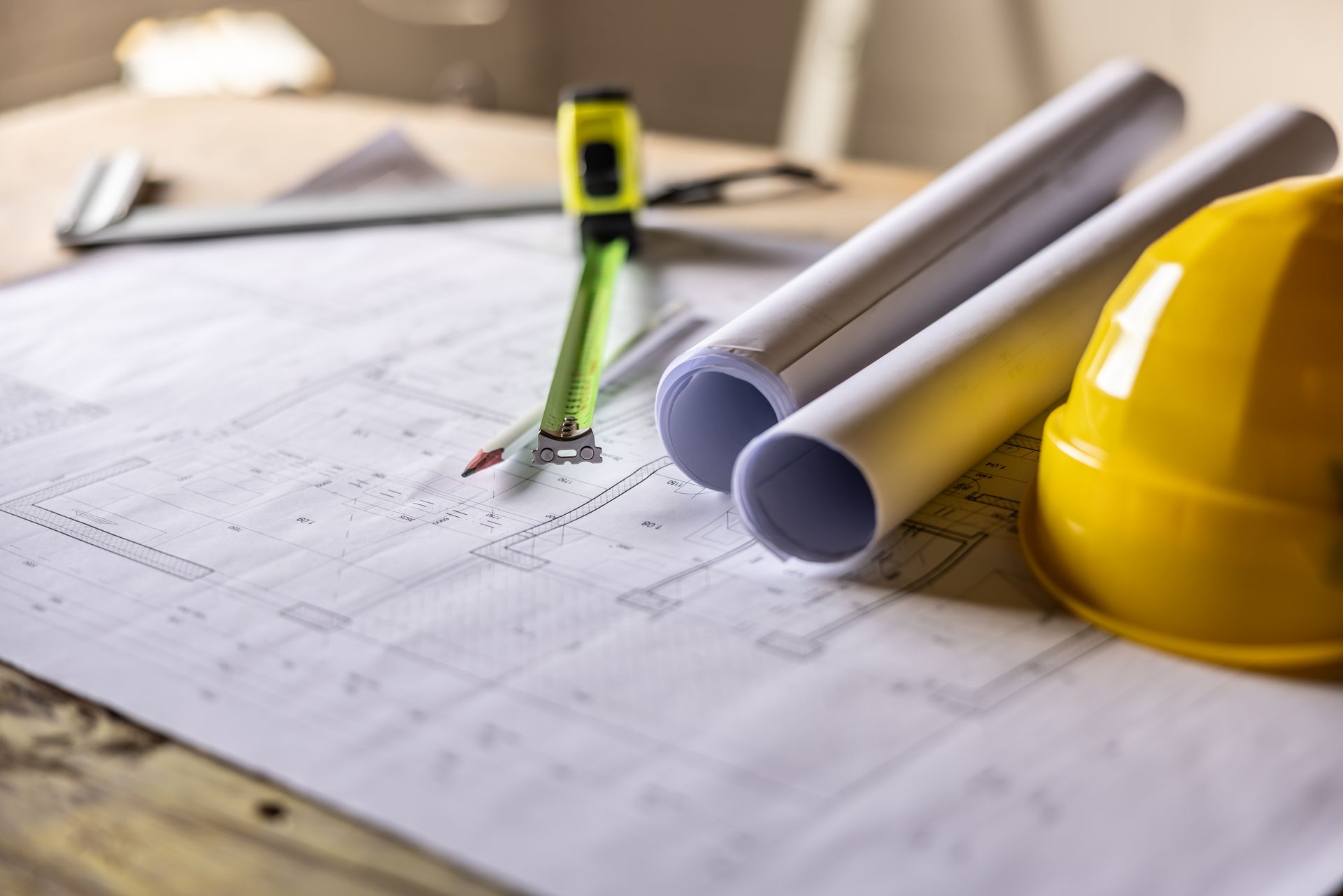 Progetto con carta arrotolata, casco giallo e metro a nastro, cantiere.