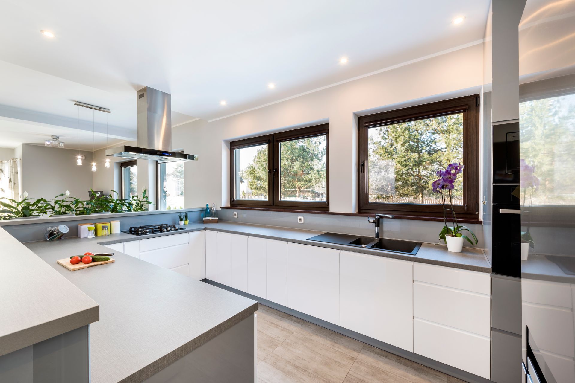 Moderna cucina bianca con ripiani grigi, cappa in acciaio inox e finestre.