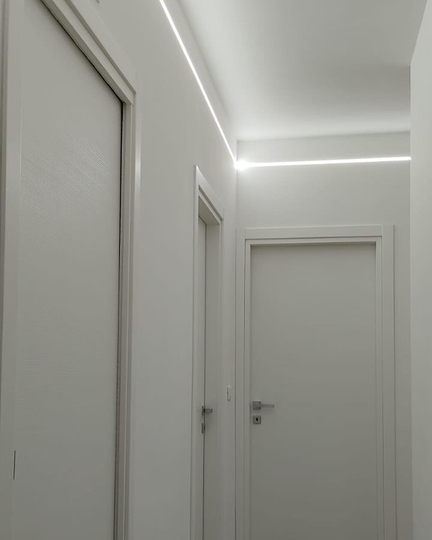 Corridoio bianco con porte e una striscia di illuminazione a LED lungo il soffitto.