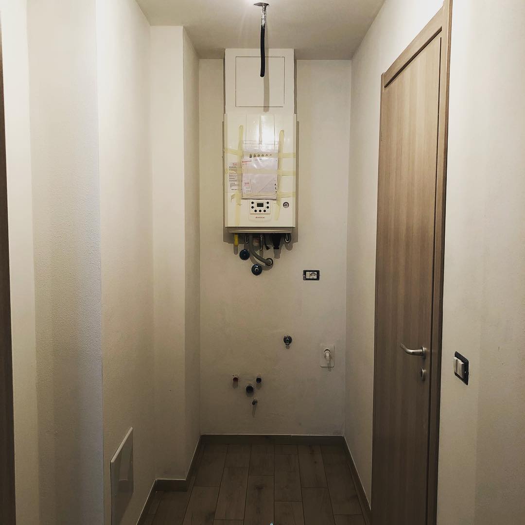 Corridoio stretto con uno scaldabagno sul muro e una porta chiusa sulla destra.