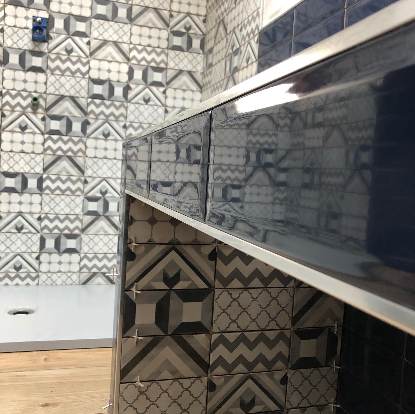Bagno con piastrelle a motivi geometrici nei toni del grigio e del blu; piano di lavoro con finiture argentate.