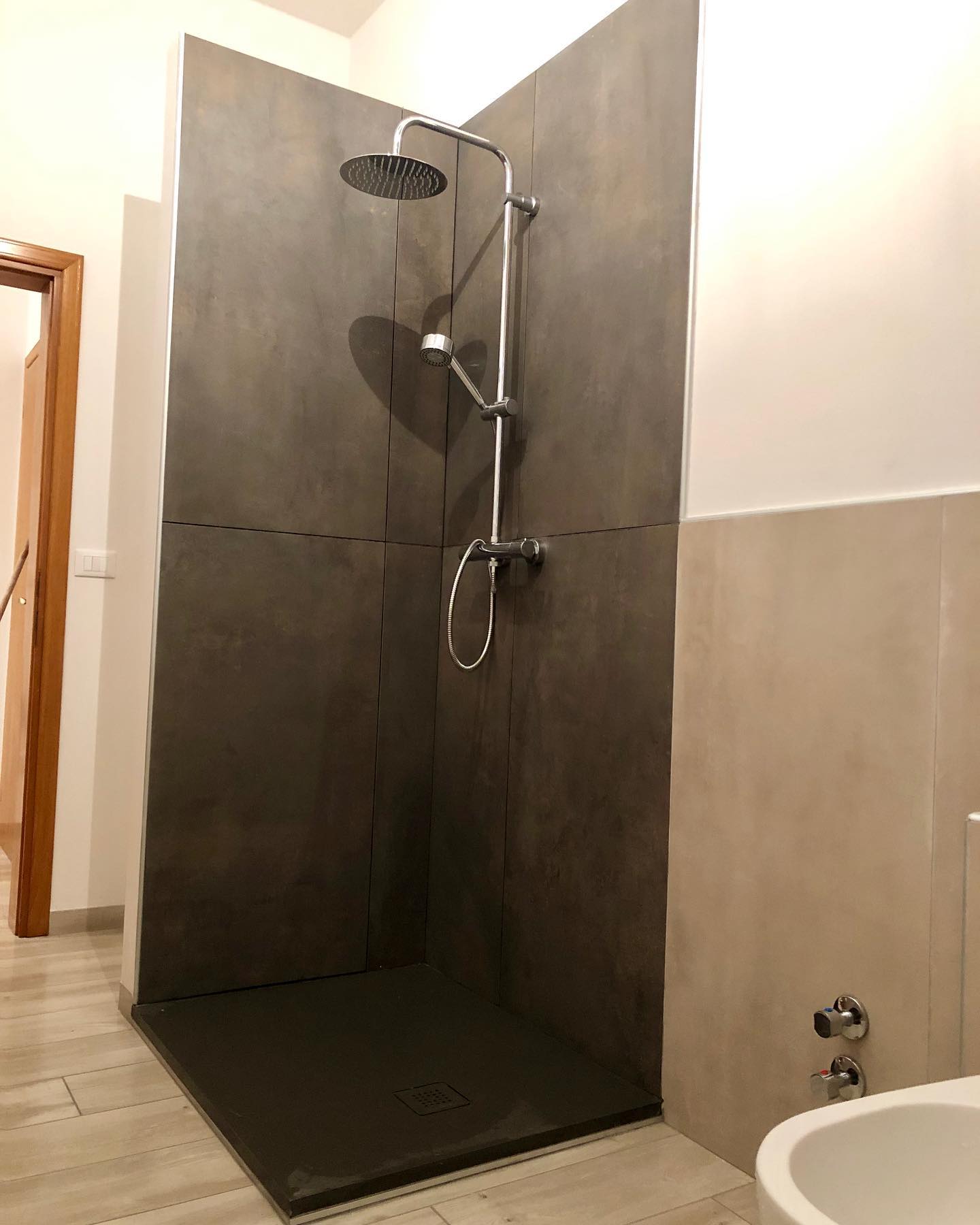 Doccia con pareti e pavimento grigio scuro; soffione e rubinetto argentati; parete beige; WC bianco.