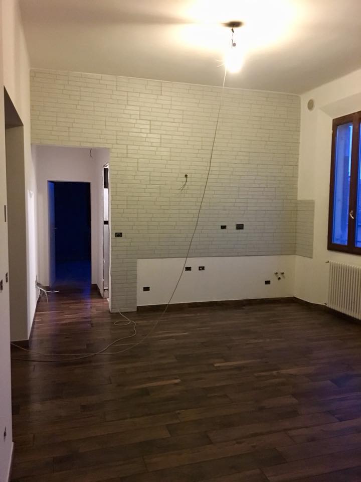 Stanza vuota con pavimenti in legno, muro di mattoni, porta aperta, finestra con tende blu.