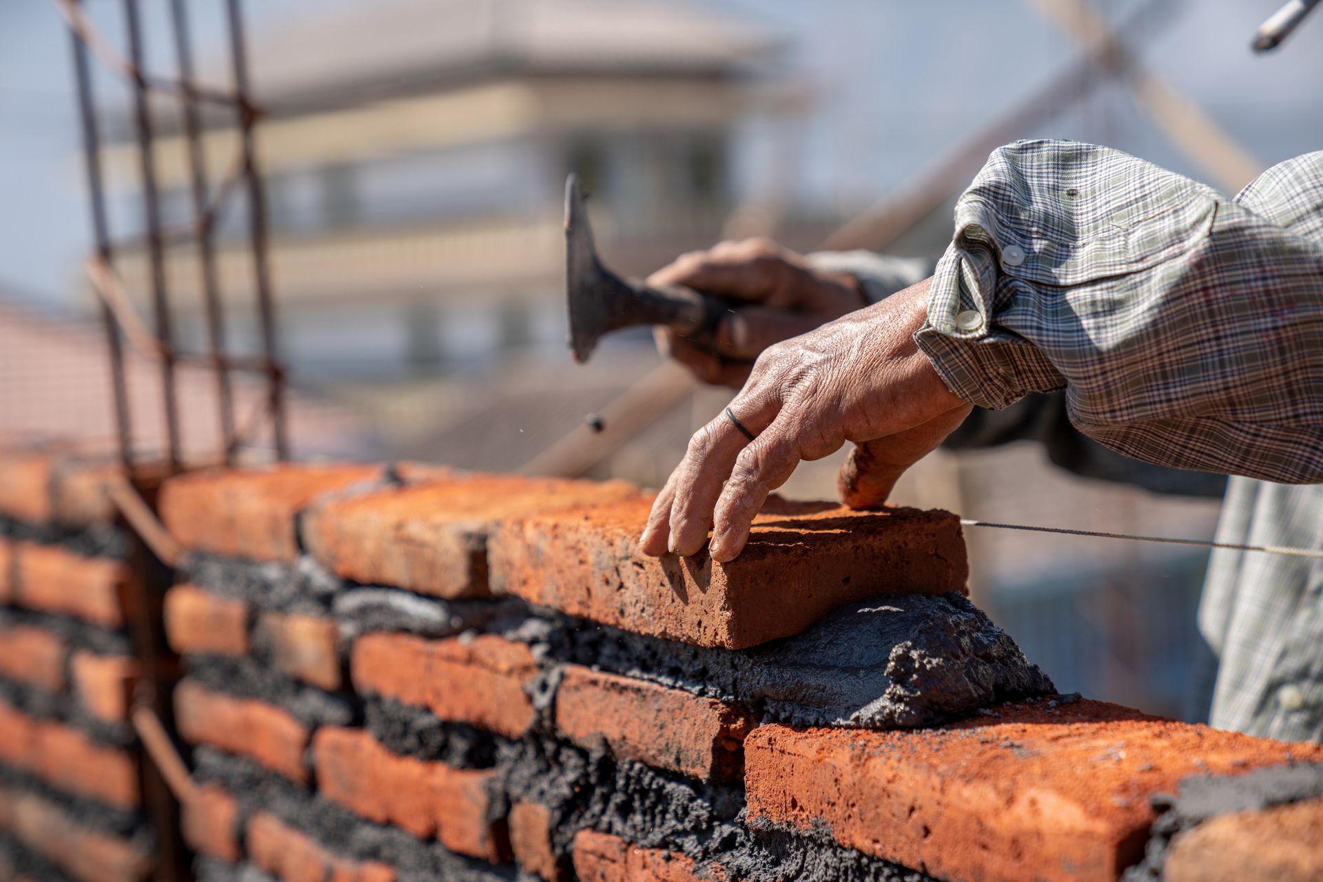 Roofer on a sloped roof wearing a hard hat, safety vest, and harness, using a drill on shingles under a cloudy sky.
