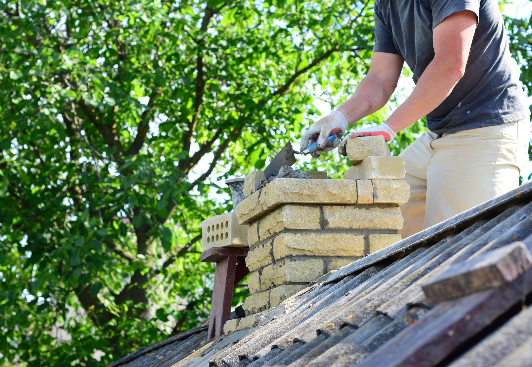 A person builds a brick chimney on a rooftop.