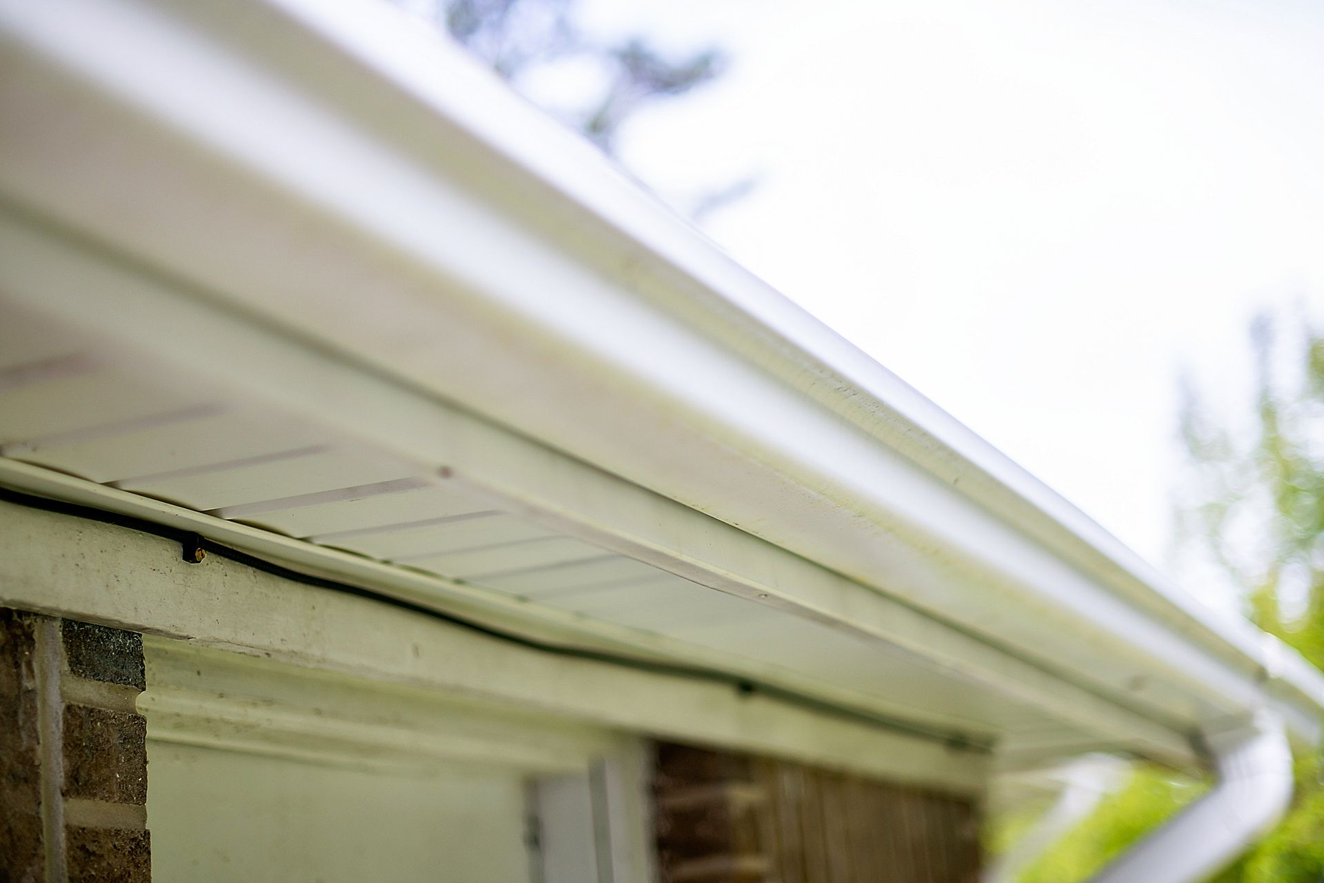 Corner of a building with red tile roof, gray gutter, and tan stucco wall against a blue sky.