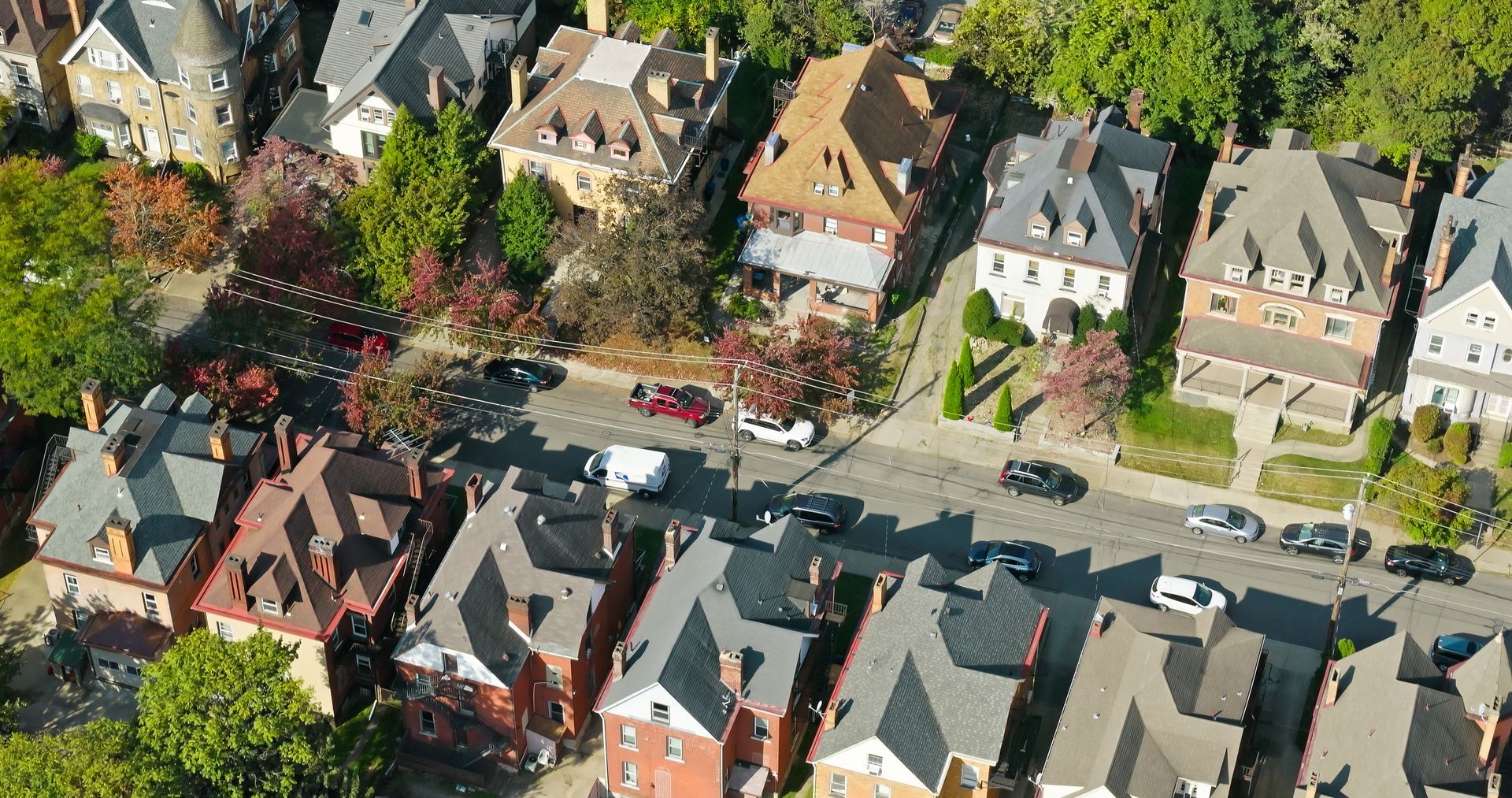 Aerial view of a street lined with multi-story brick houses and cars, trees on the sidewalks.
