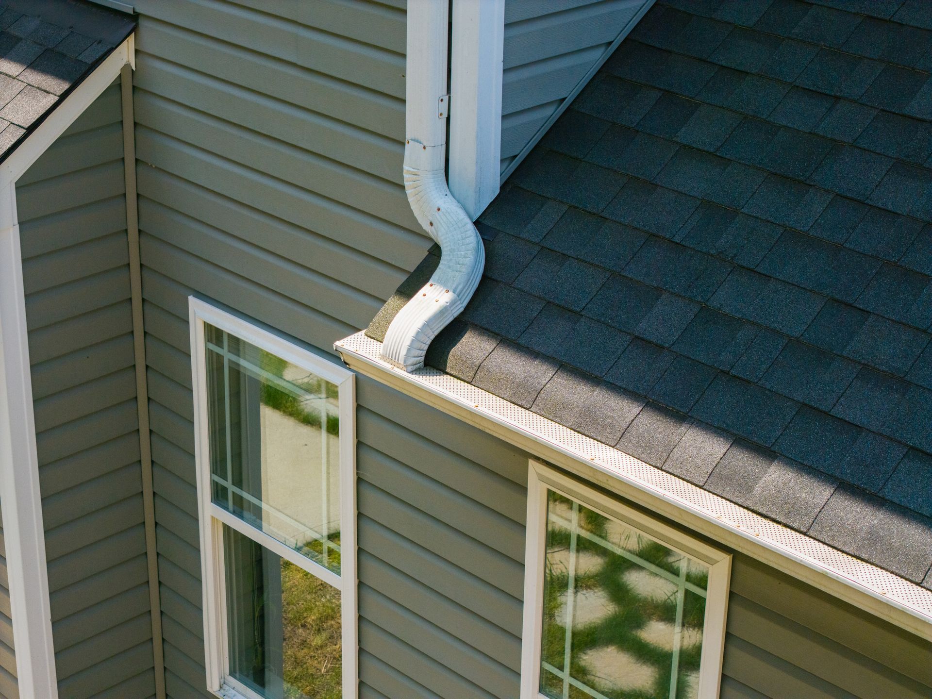 White gutters attached to a white soffit on a building with terracotta roof tiles against a cloudy sky.