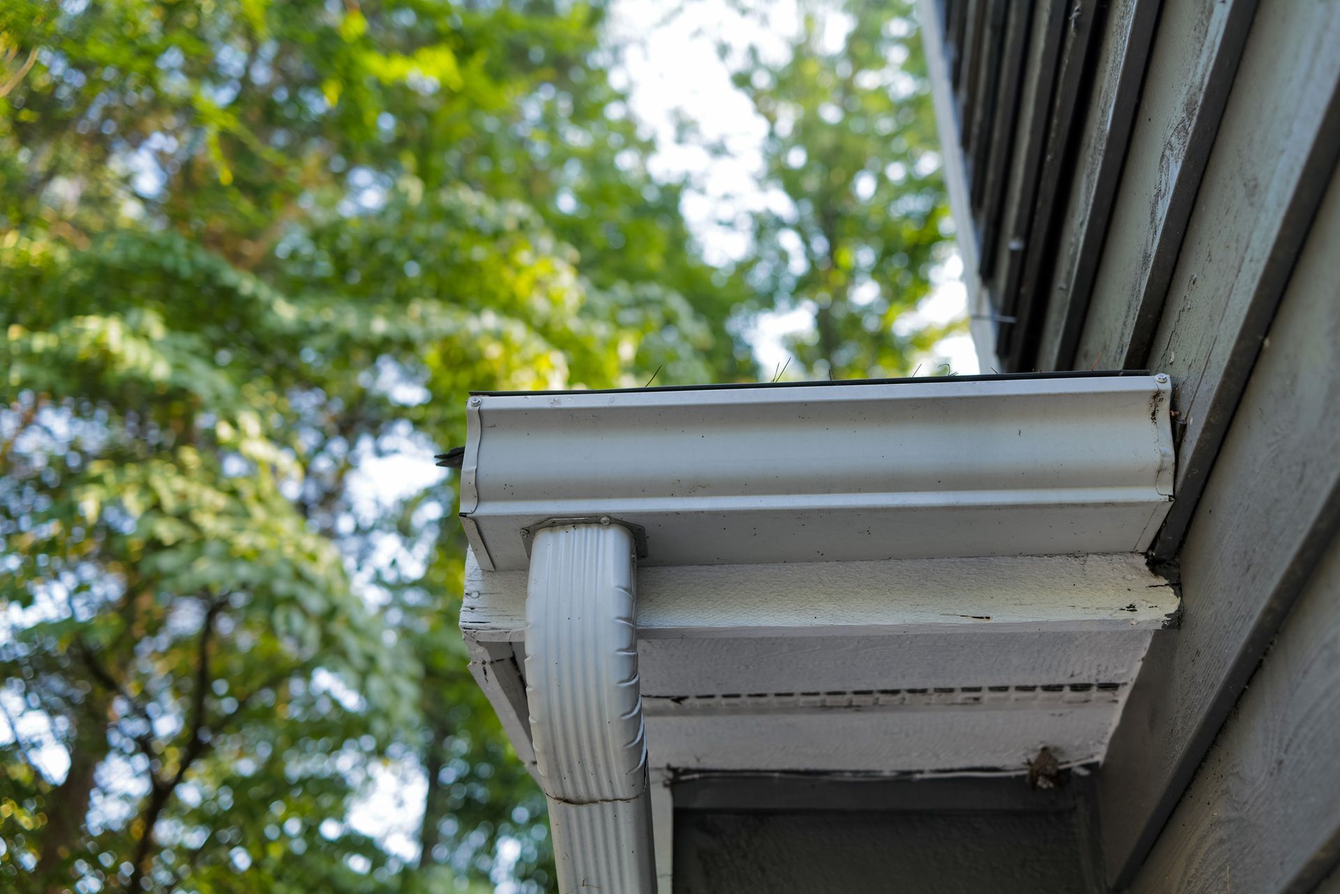 White gutters attached to a white soffit on a building with terracotta roof tiles against a cloudy sky.