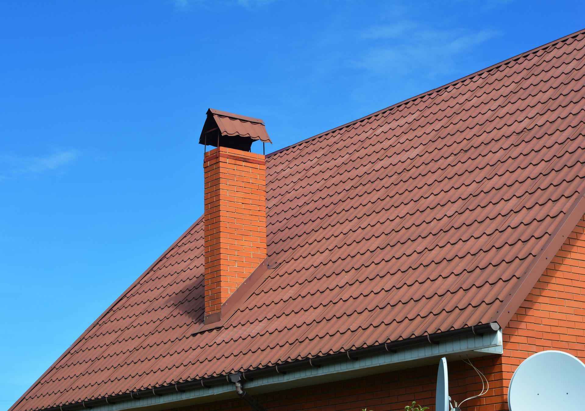 Two roofers in hard hats and vests working on a clay tile roof.