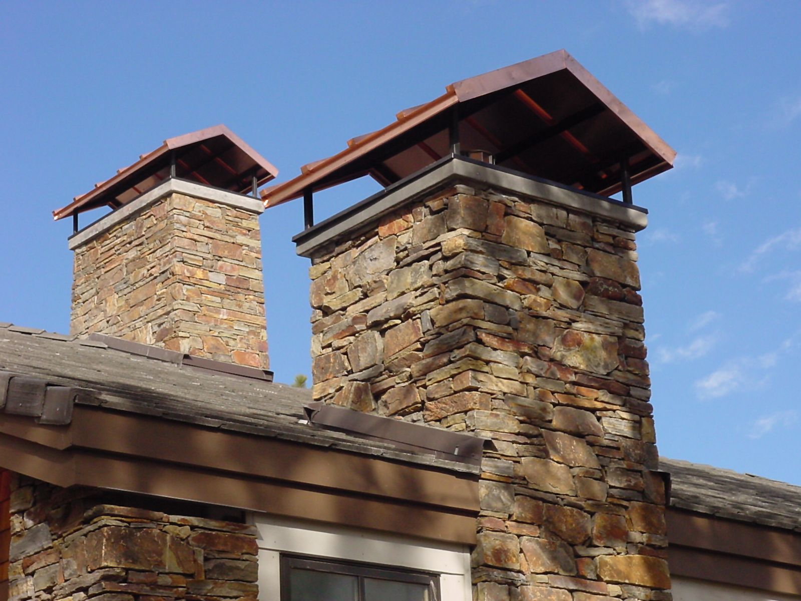 Two stone chimneys with copper caps against a blue sky.