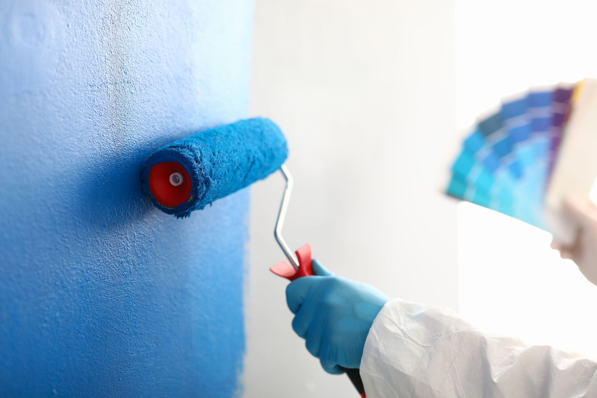 A person is painting a wall with a blue paint roller.