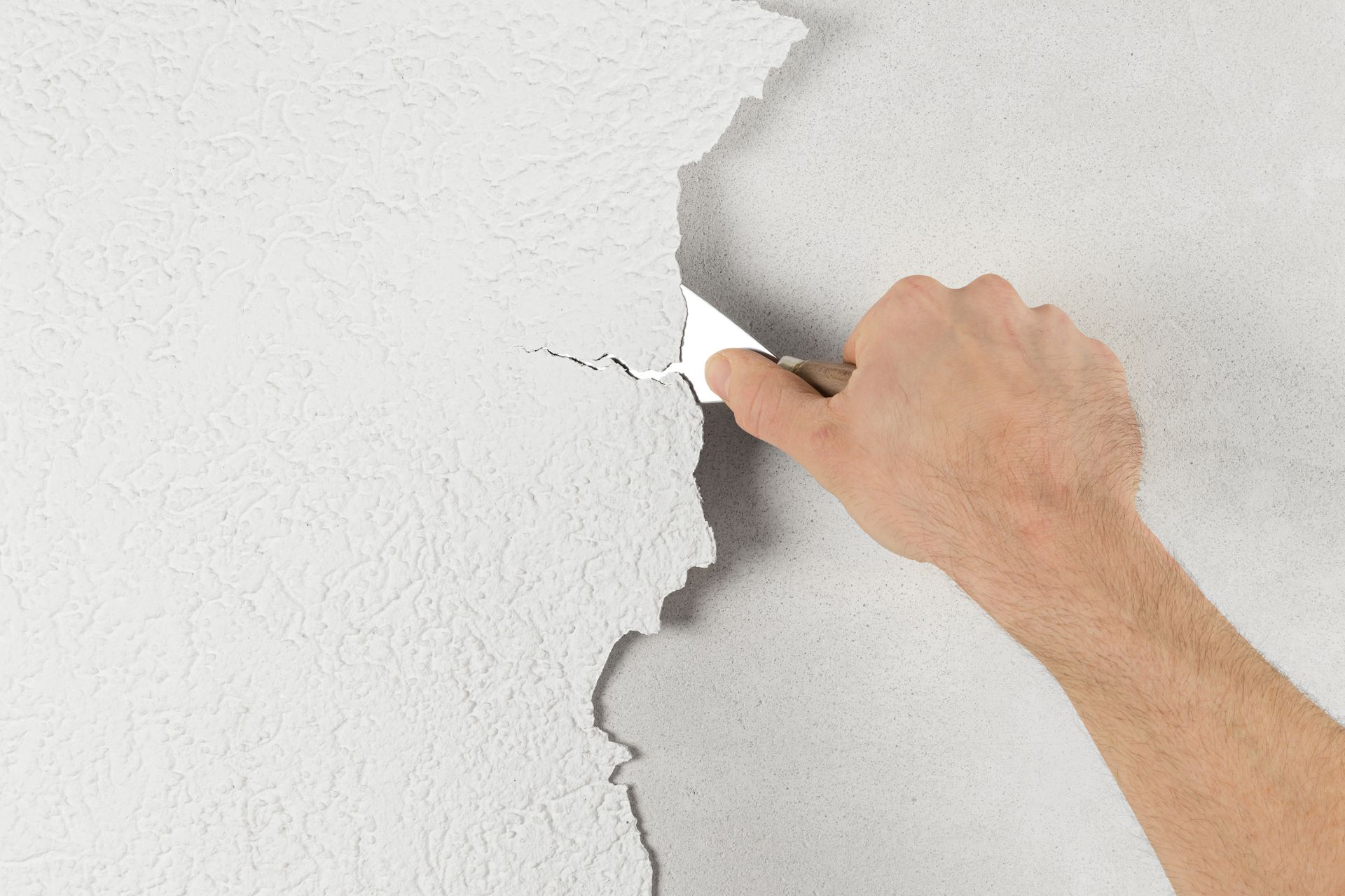 A person is peeling off a white wall with a spatula.