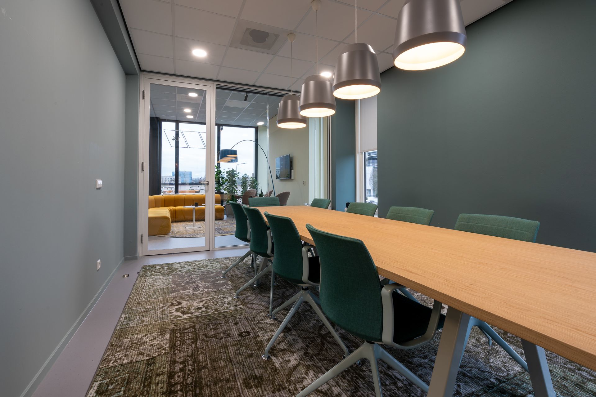 A conference room with a long wooden table and green chairs.