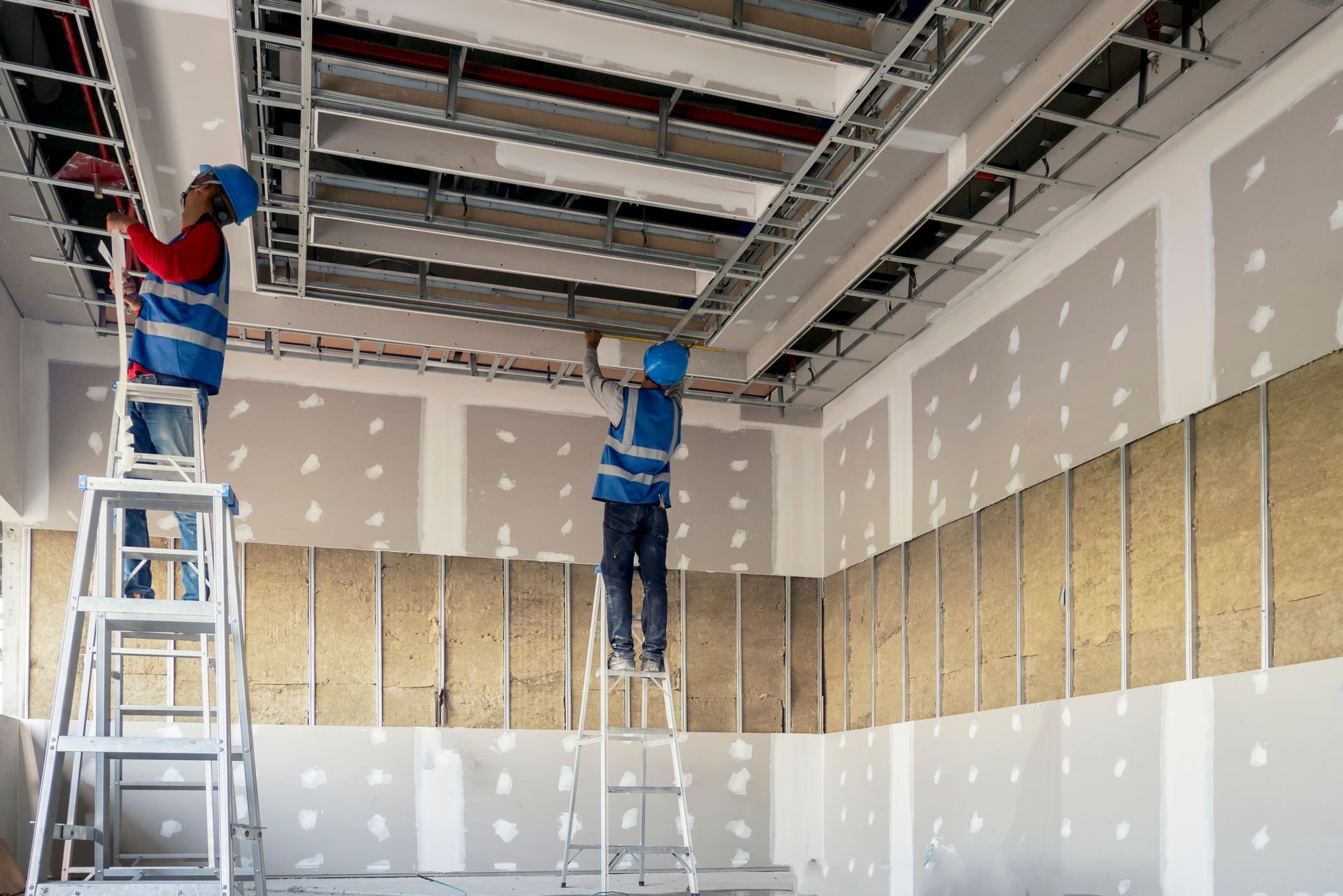 Two construction workers are working on the ceiling of a building.