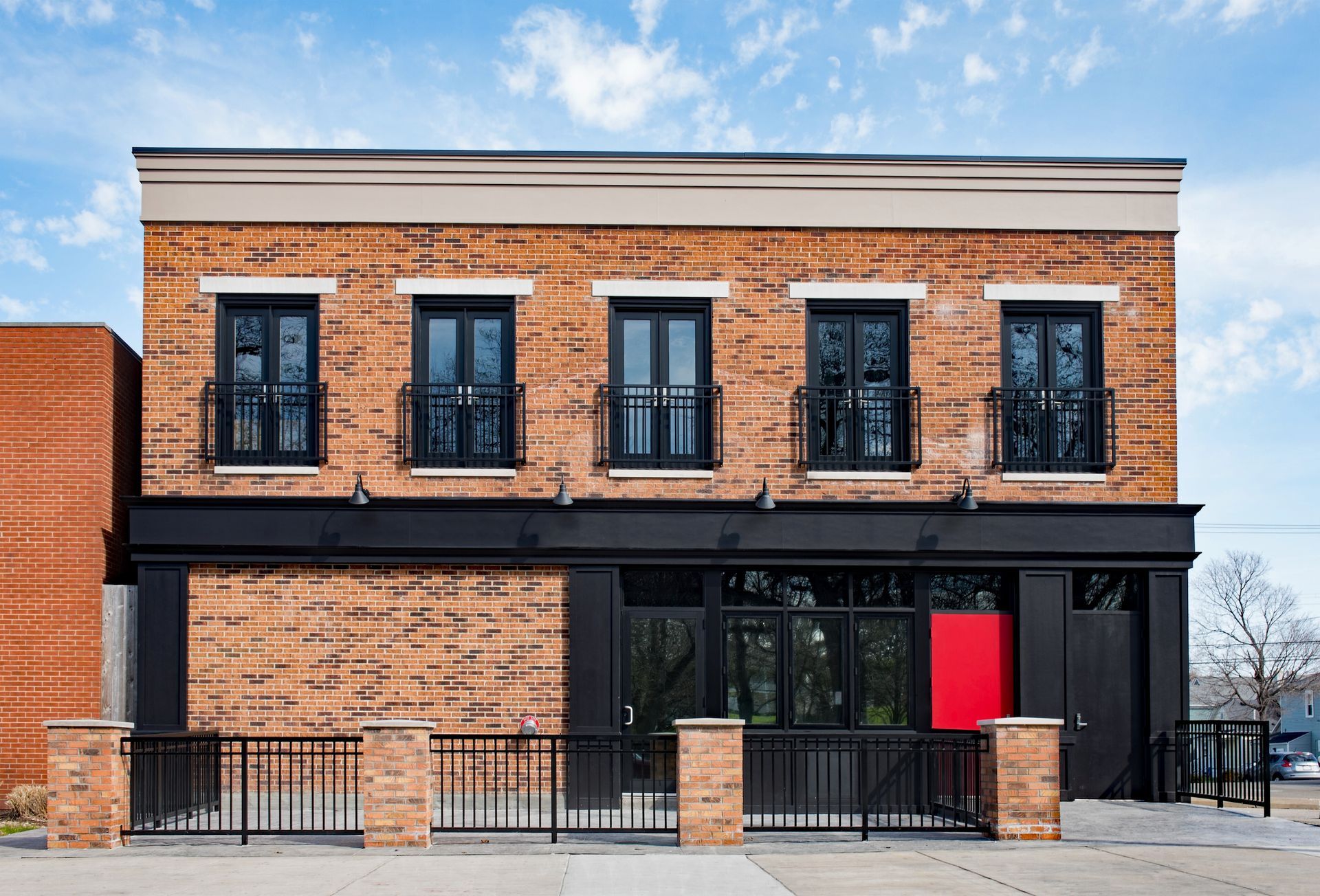 A brick building with black windows and a red door