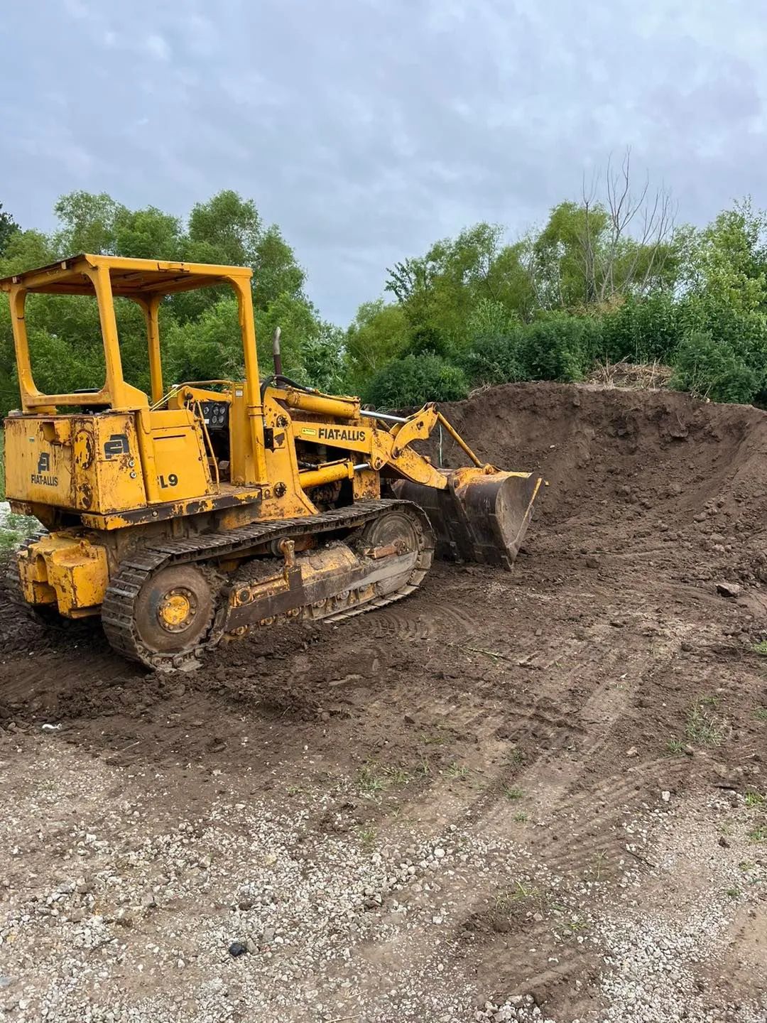 Yellow tracked bulldozer moving dirt on a cloudy day.