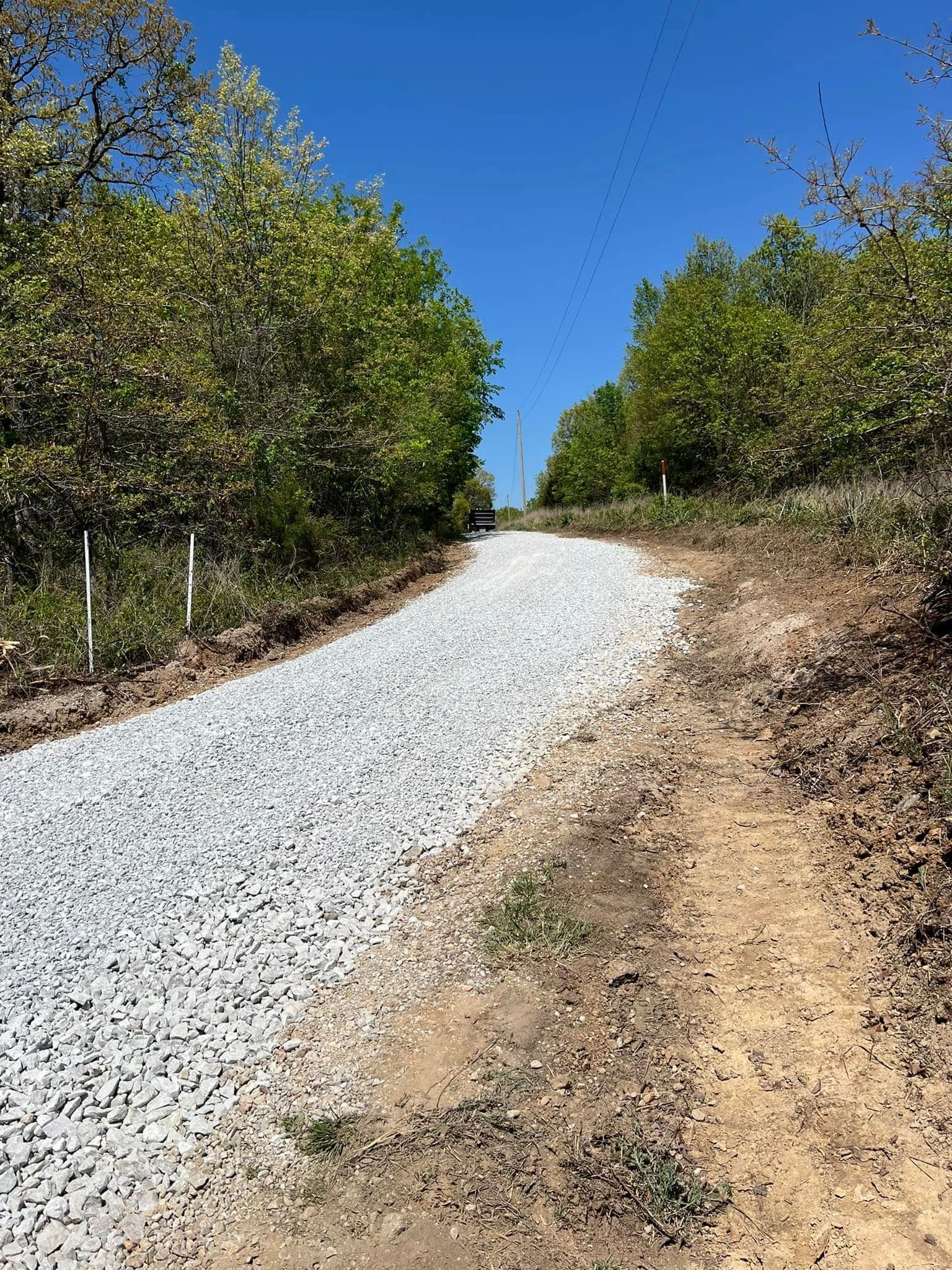 Gravel path through a wooded area, sunny day, blue sky.